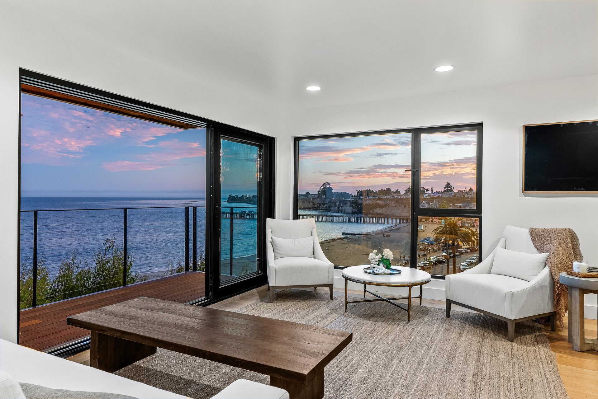 Modern living room with floor-to-ceiling windows, ocean view, white chairs, and a wooden coffee table