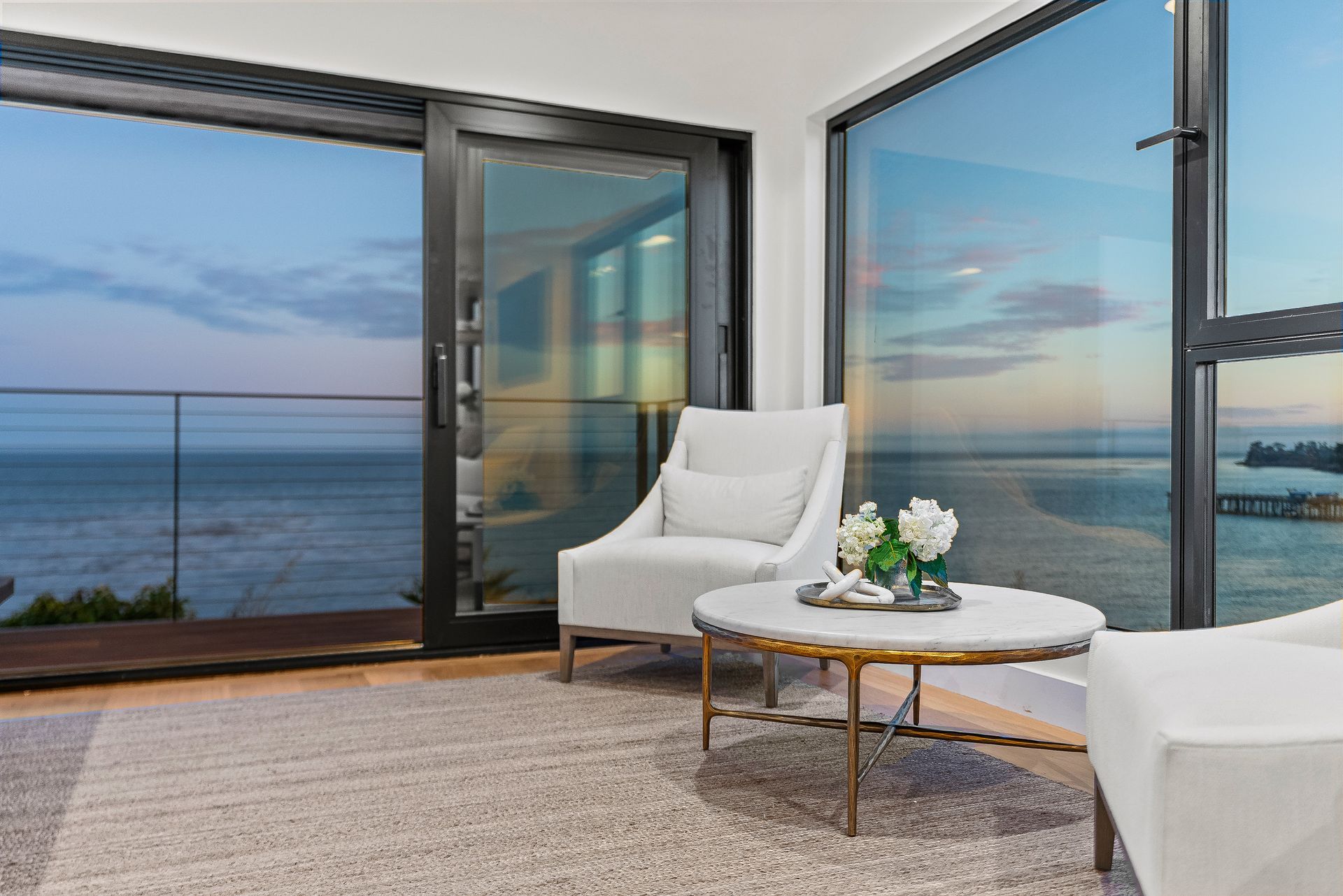 Modern patio with white chairs and a small table overlooking the ocean at sunset