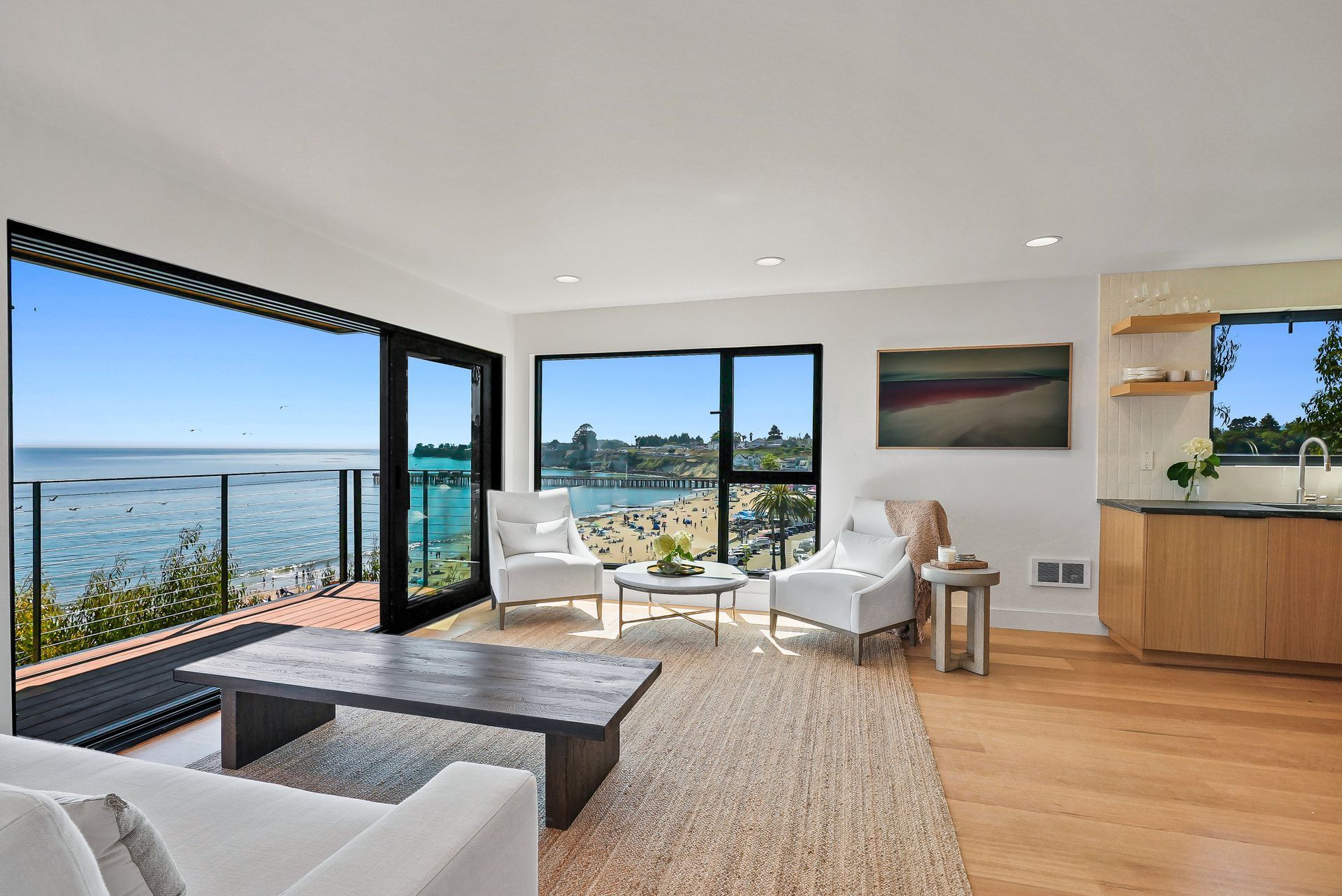 Modern living room with ocean view, floor-to-ceiling windows, white chairs, and a dark coffee table