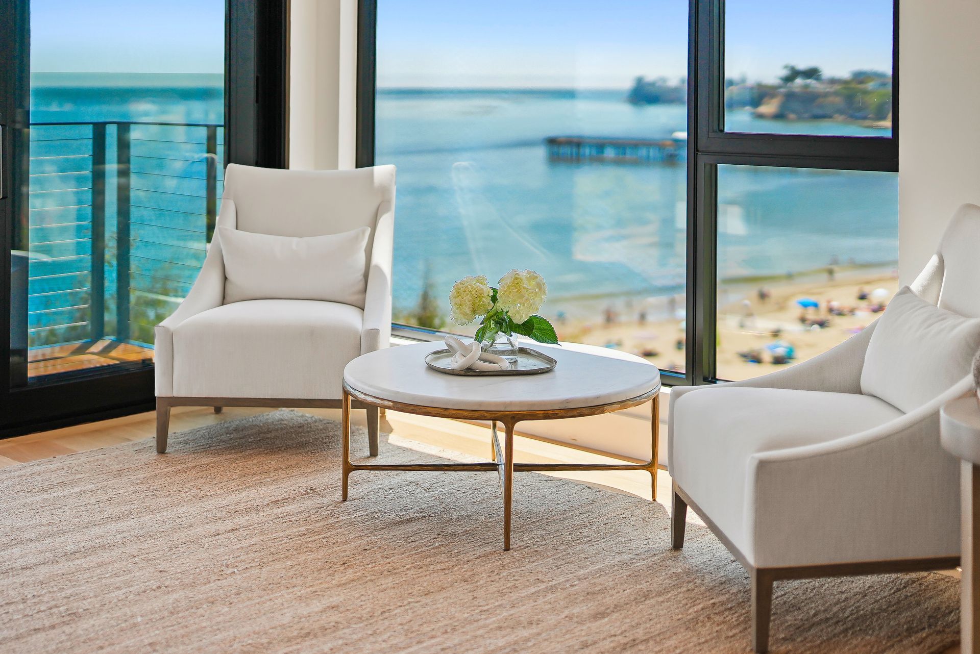 Bright living room with white chairs and ocean-view windows overlooking a beach