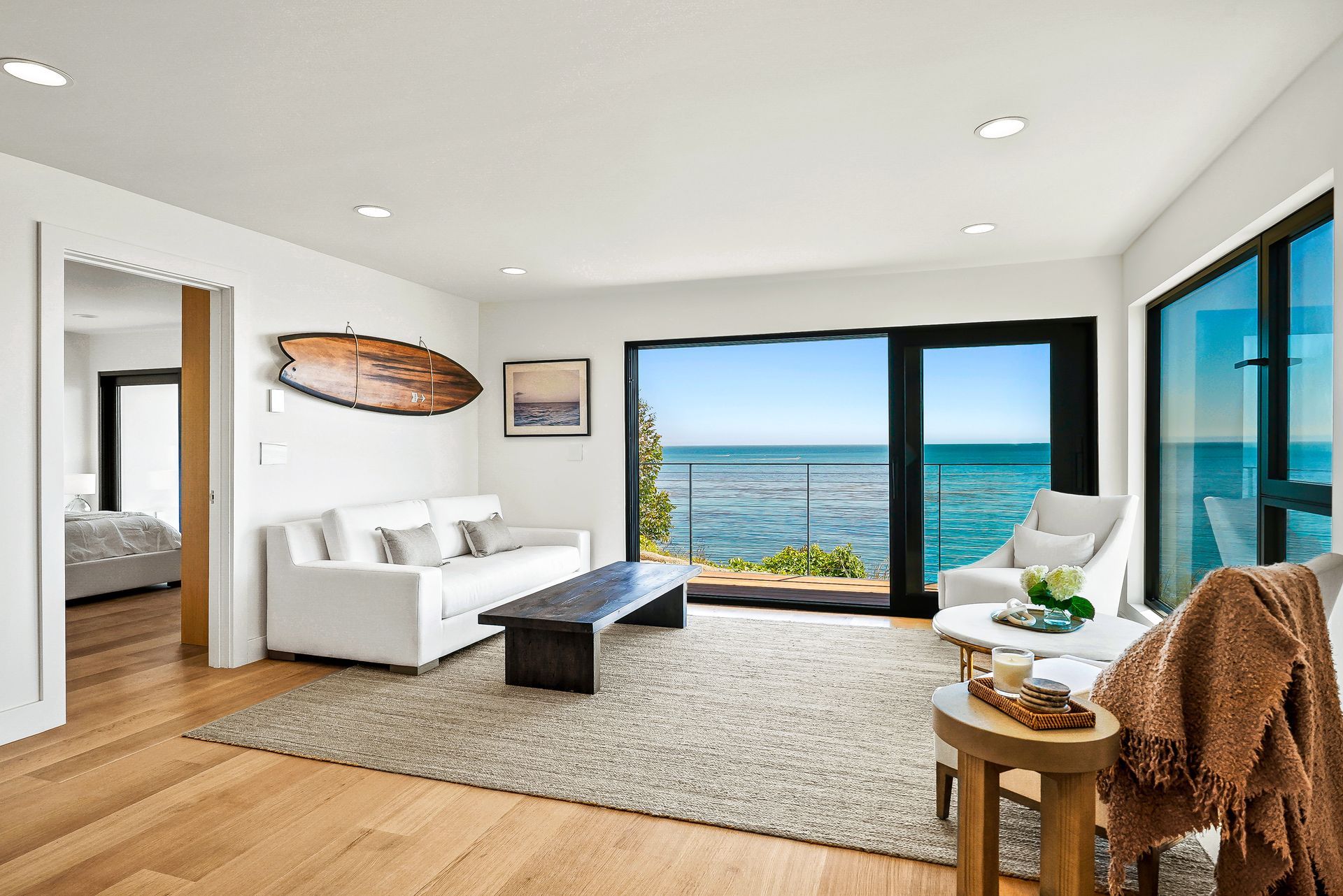 Bright living room with ocean view, white sofa, rug, coffee table, and sliding glass doors.