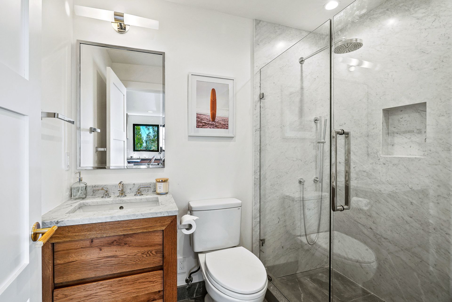 Modern bathroom with wood vanity, white toilet, and glass-enclosed shower.