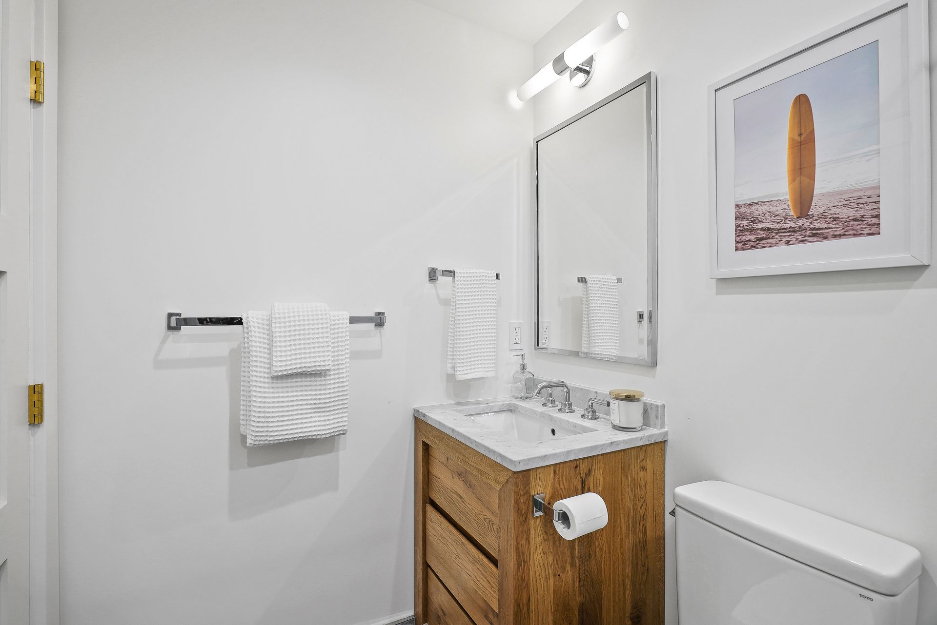Bright bathroom with wooden vanity, mirror, white towel, and framed wall art