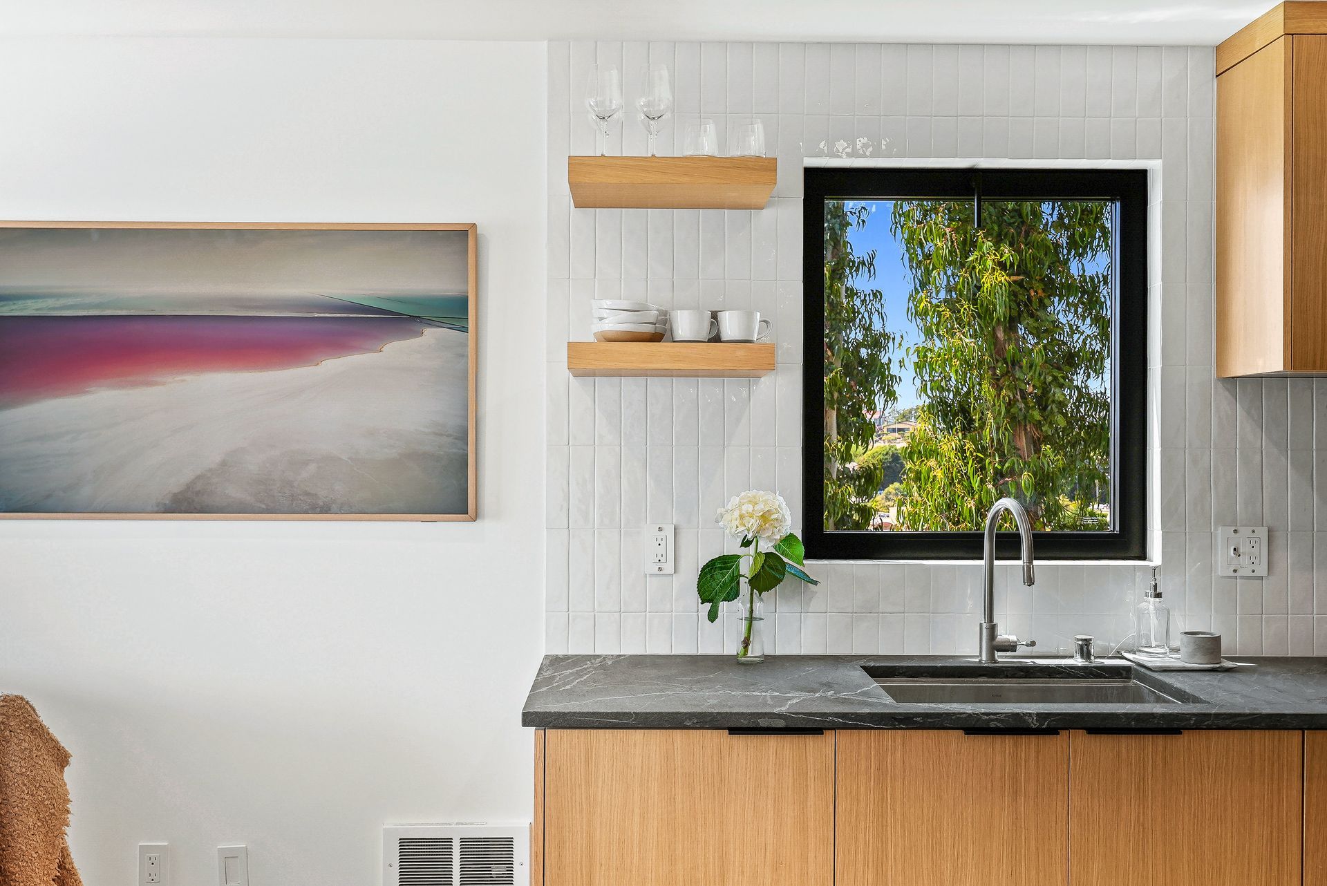 Modern kitchen with wooden cabinets, granite countertop, sink under window, and wall art