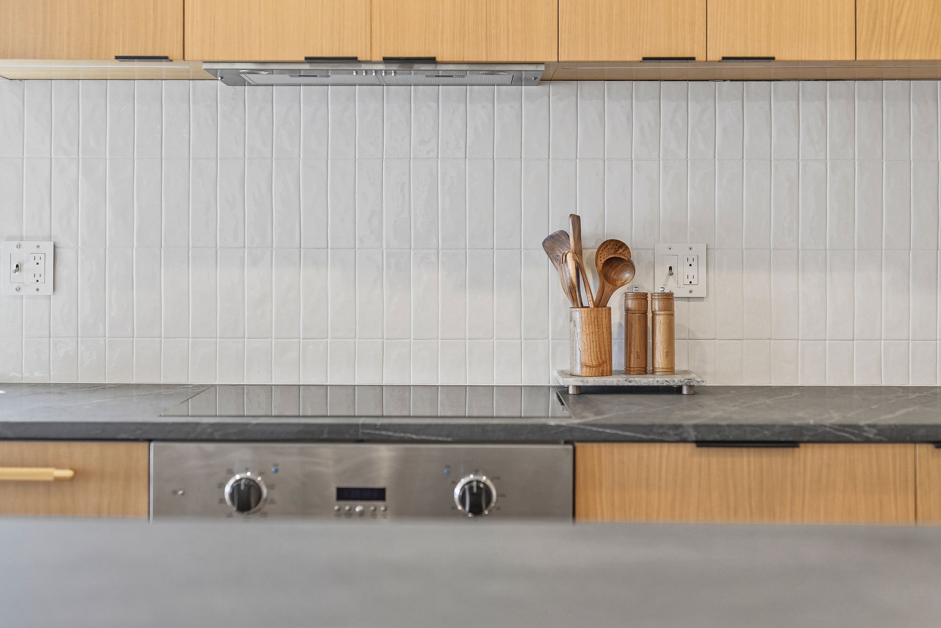 Modern kitchen with light wood cabinets, white tiled backsplash, and utensils on the countertop