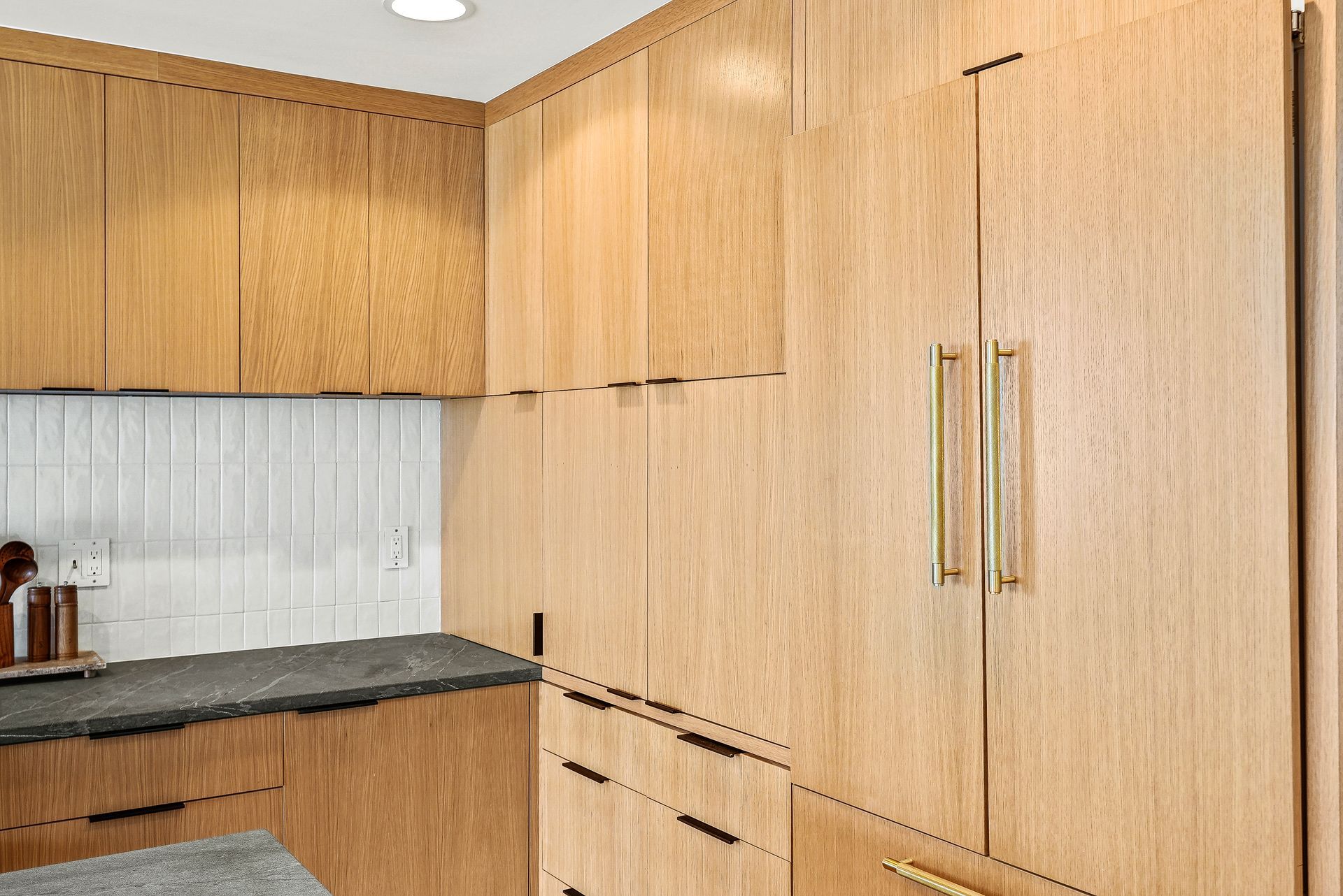 Wood-paneled kitchen with white tile backsplash, gray countertop, and built-in cabinets and drawers