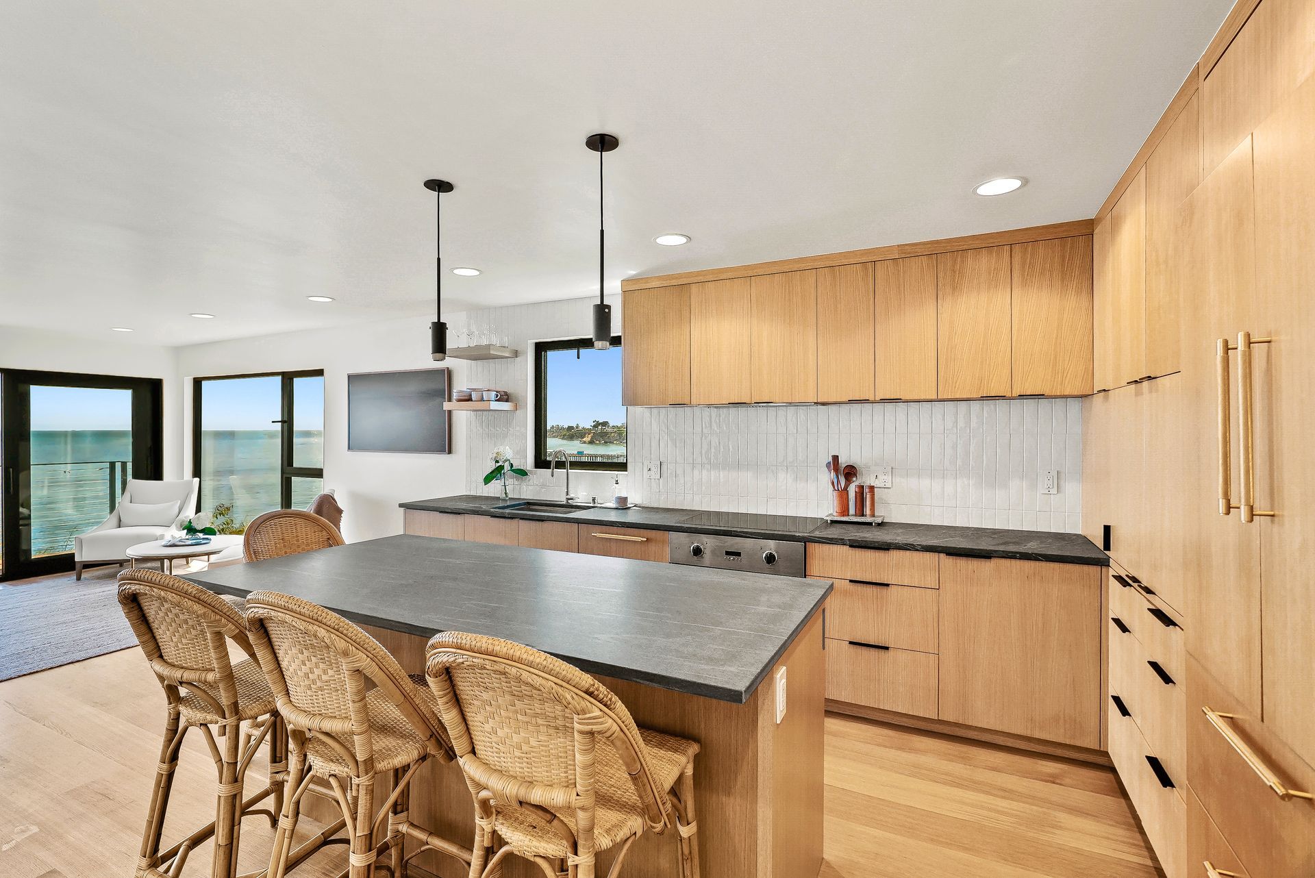Modern kitchen with island, wicker barstools, wood cabinets, and large windows overlooking a view.