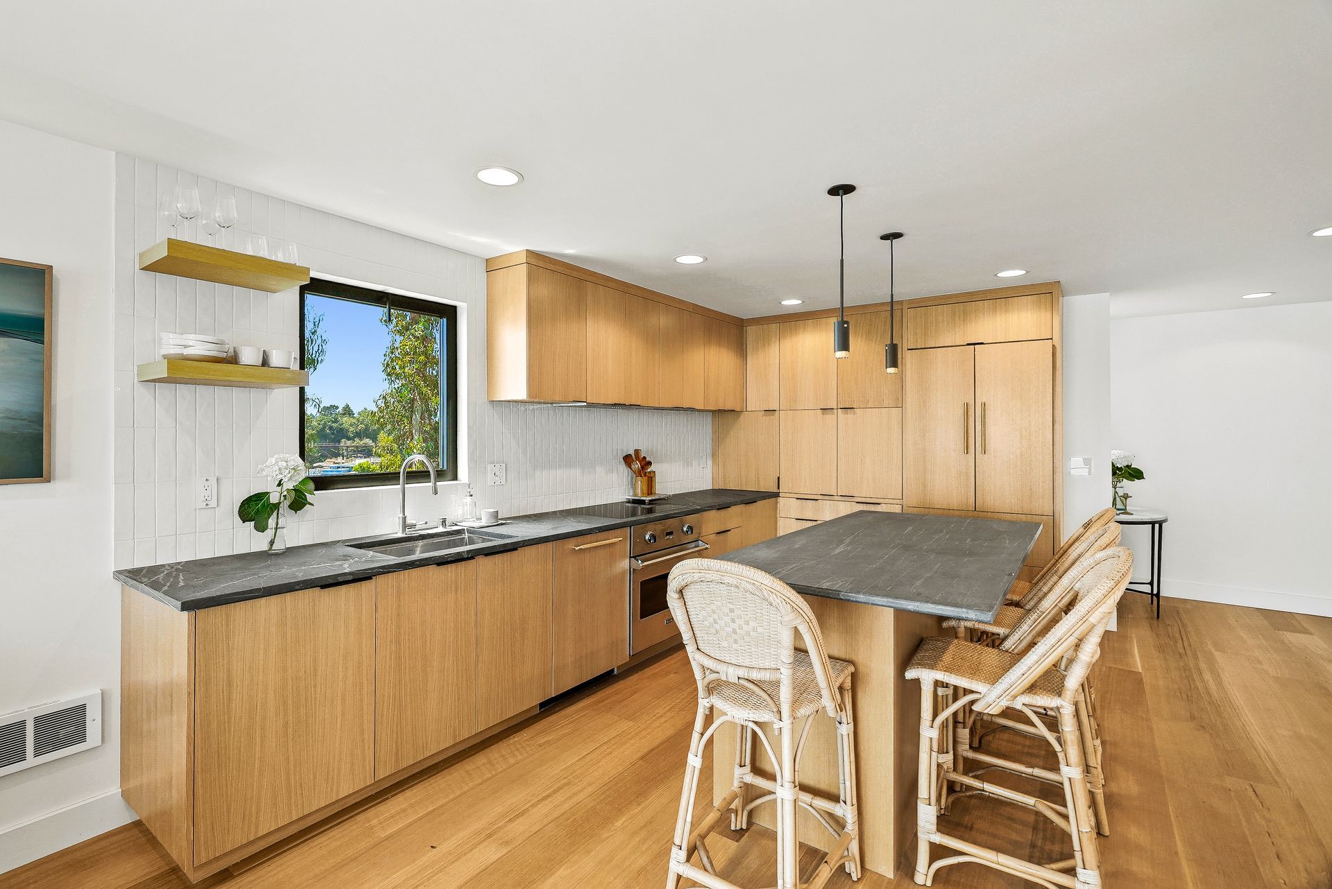 Bright modern kitchen with wood cabinets, granite island, and wicker bar stools under pendant lights