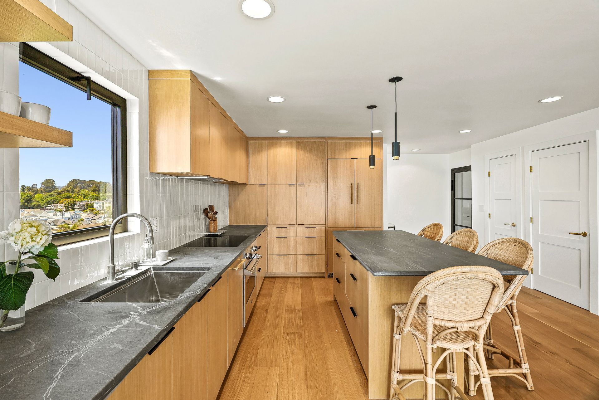 Bright modern kitchen with island, wood cabinets, black countertops, and wicker bar stools