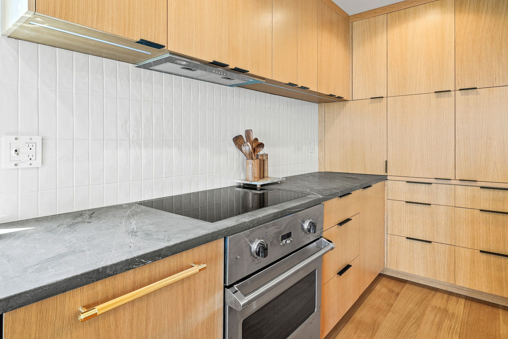 Modern kitchen with light wood cabinets, gray countertops, and a built-in stainless steel oven.
