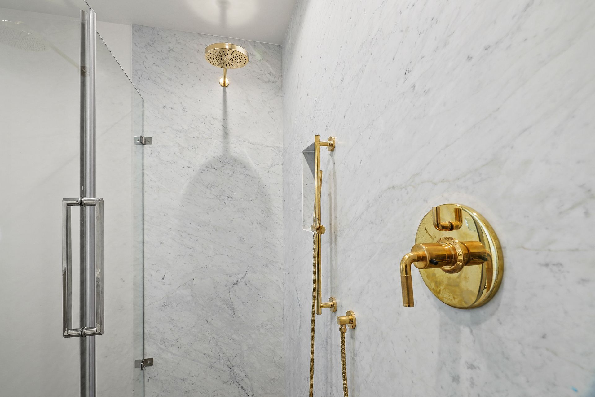 Gold shower fixtures in a white marble-tiled bathroom shower stall