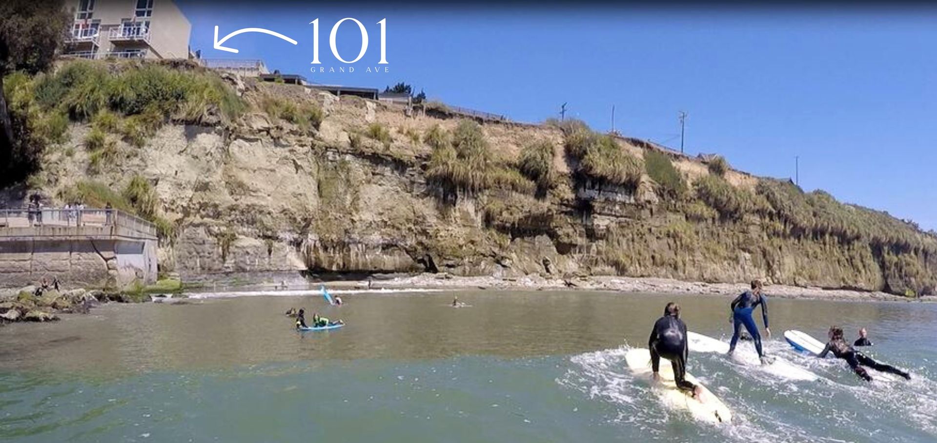 People surfing near rocky cliffs and a coastal fort under a blue sky