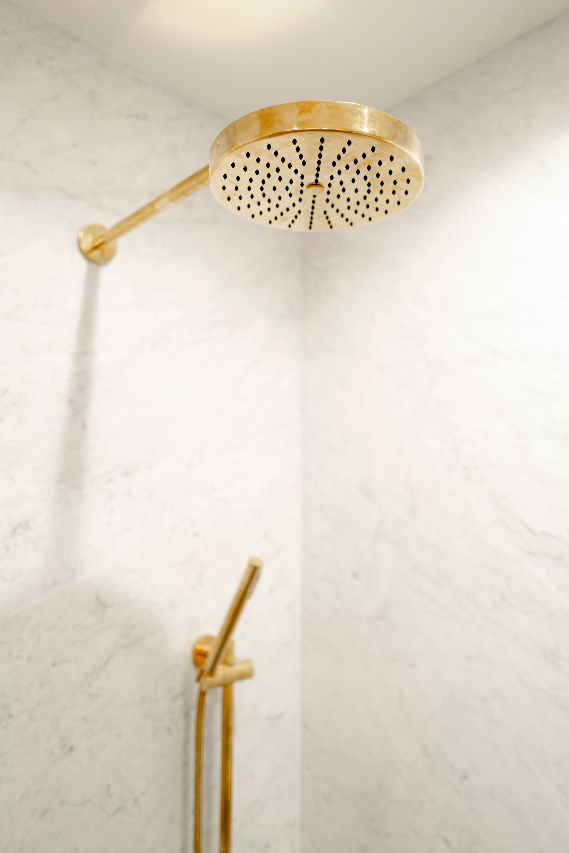 Gold showerhead and faucet in a white-tiled bathroom shower
