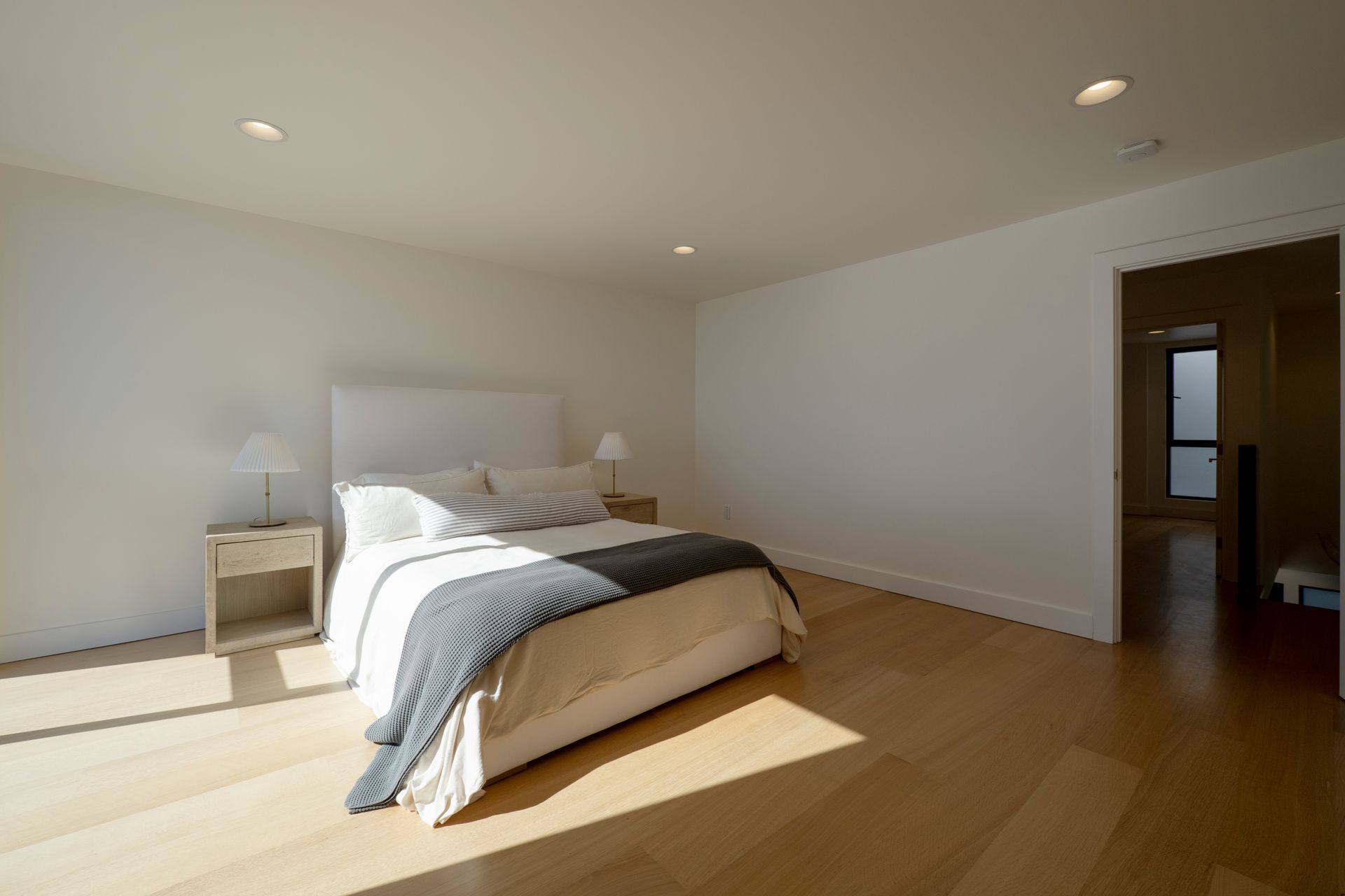 Minimal bedroom with a bed, nightstands, wood floor, and bright sunlight from the left