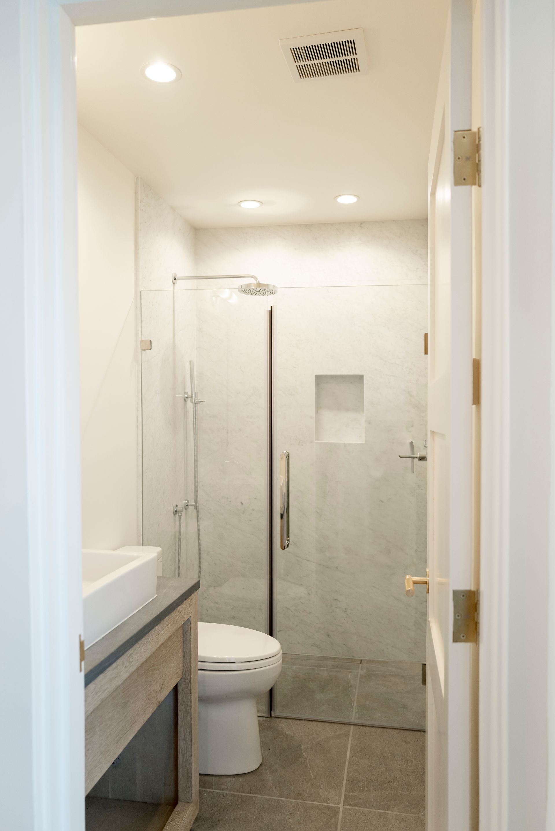 Small white bathroom with gray tile, a sink, toilet, and glass shower door.