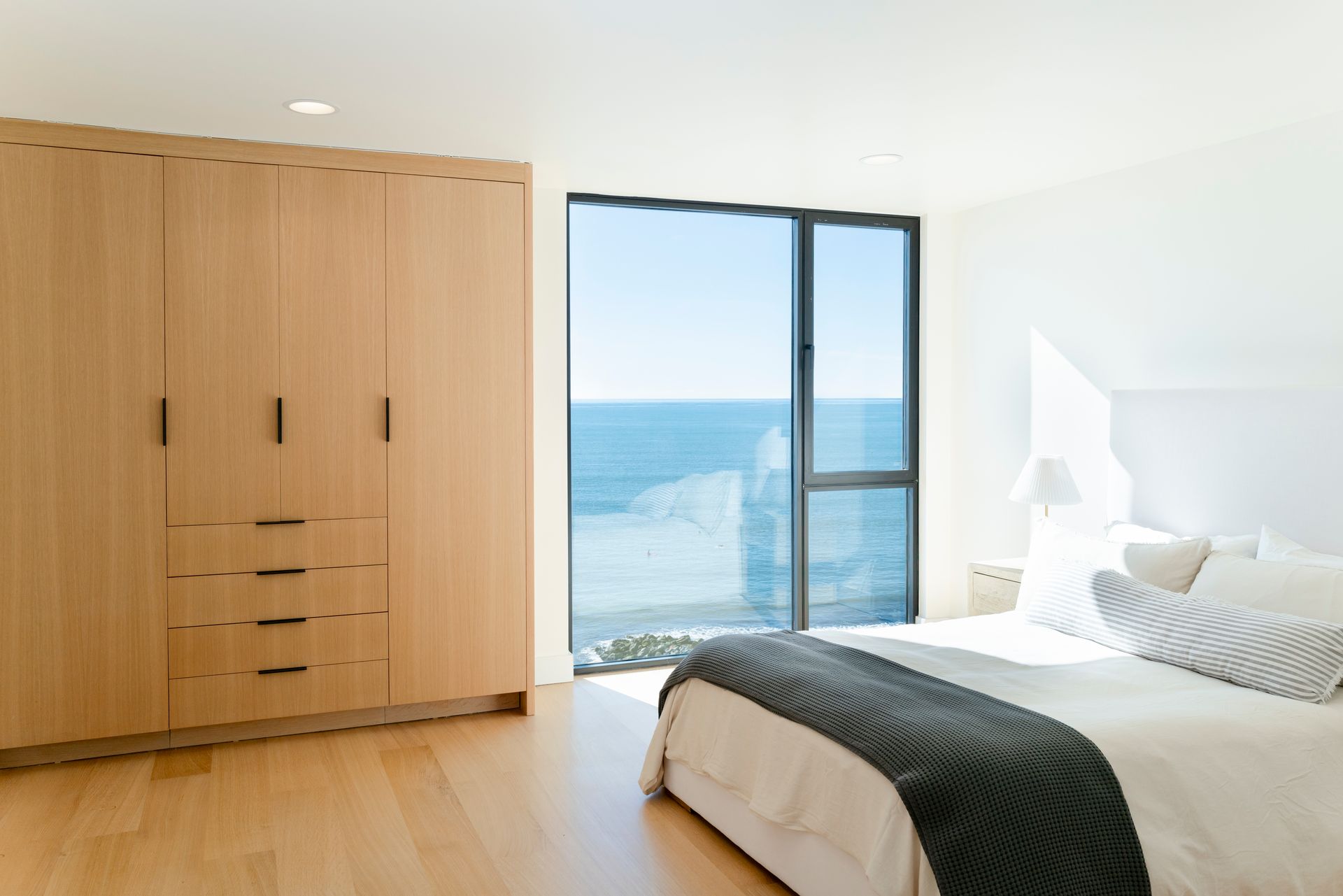 Bright bedroom with bed, wooden wardrobe, and ocean view through large windows