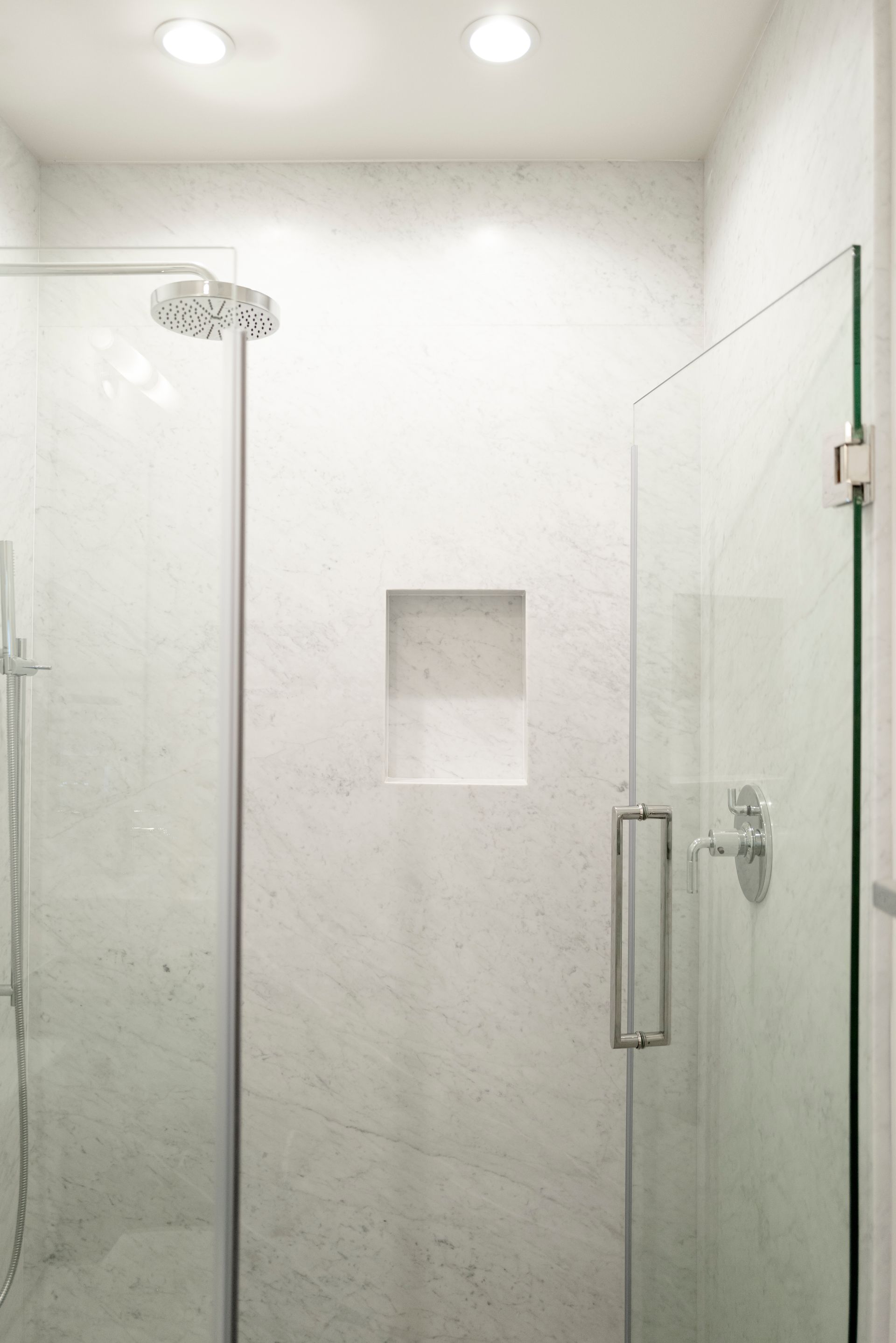 Modern glass shower with white tile, overhead lights, and a recessed wall niche