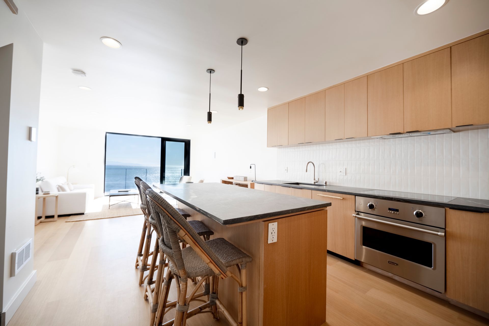 Bright modern kitchen with island, bar stools, wood cabinets, and large windows overlooking water
