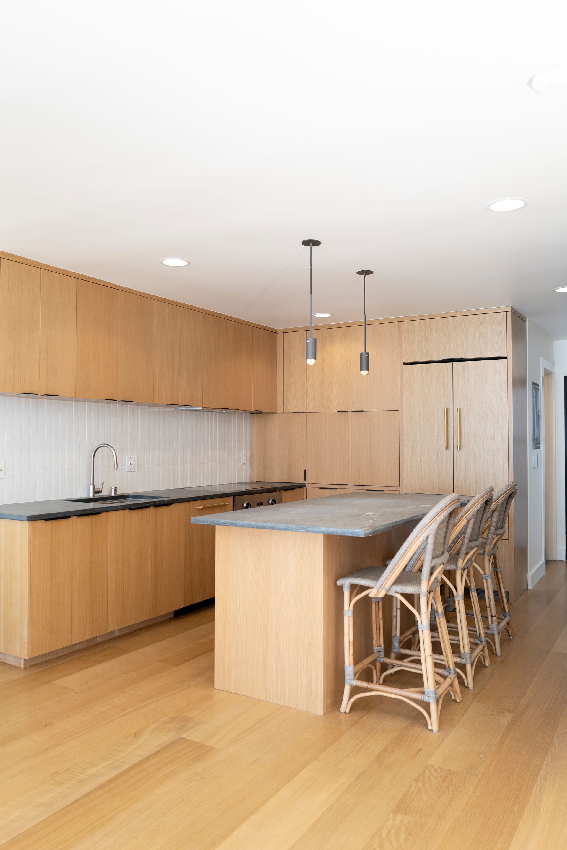 Modern kitchen with light wood cabinets, island, and woven bar stools on a wood floor