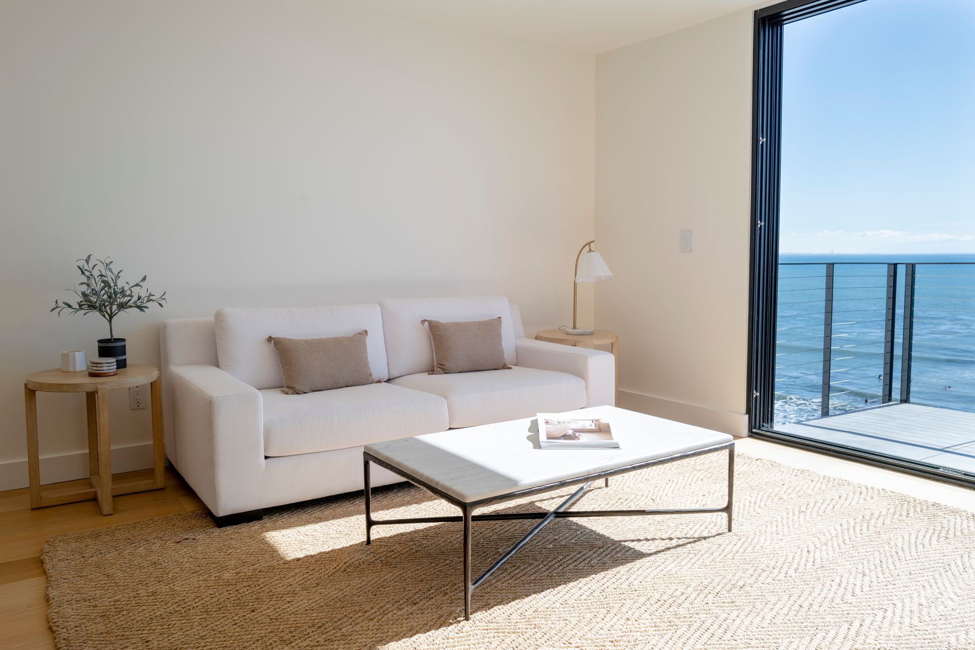 Bright living room with white sofa, coffee table, and ocean view through open balcony doors