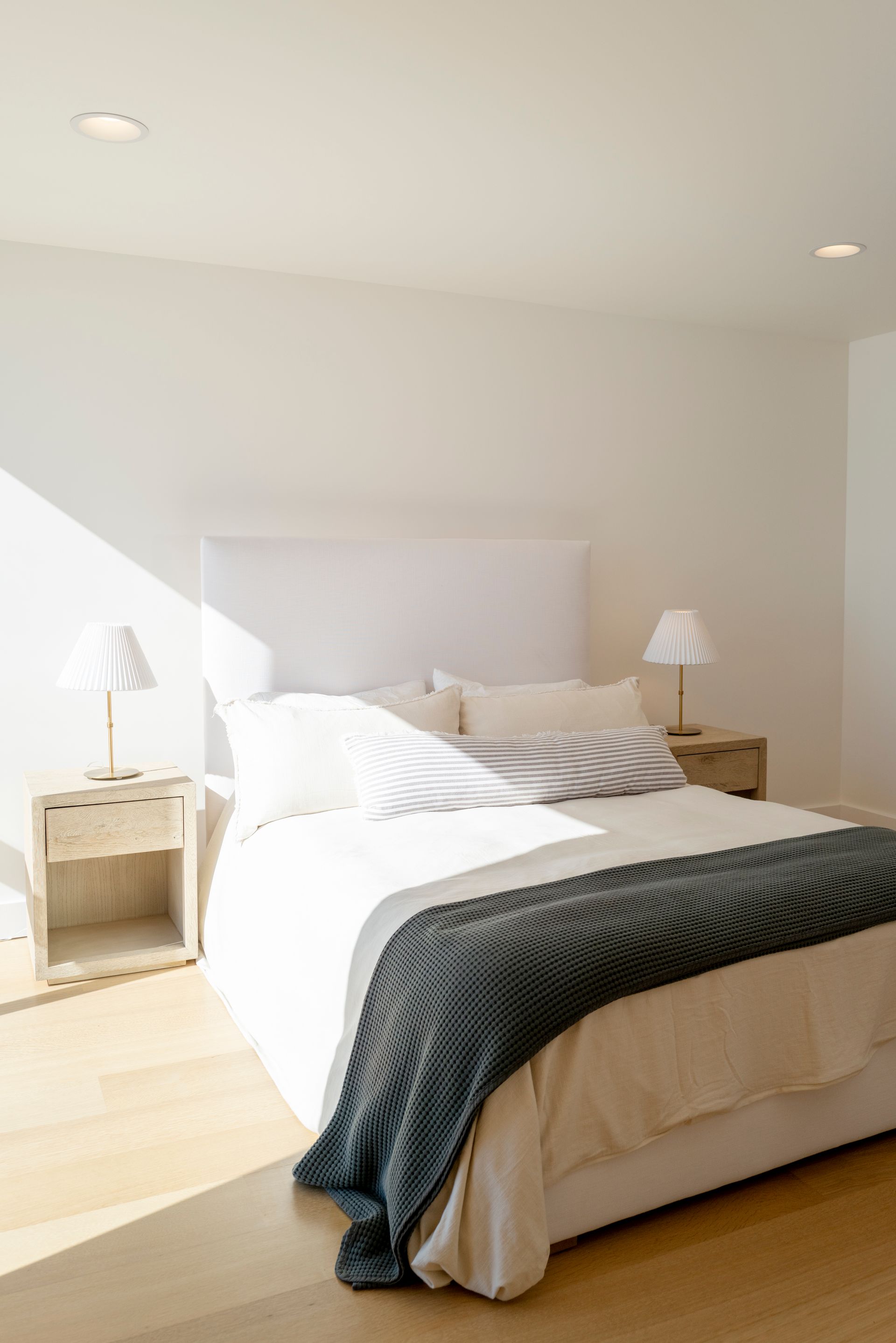 Bright minimalist bedroom with white bed, bedside tables, and sunlight on pale wood floor