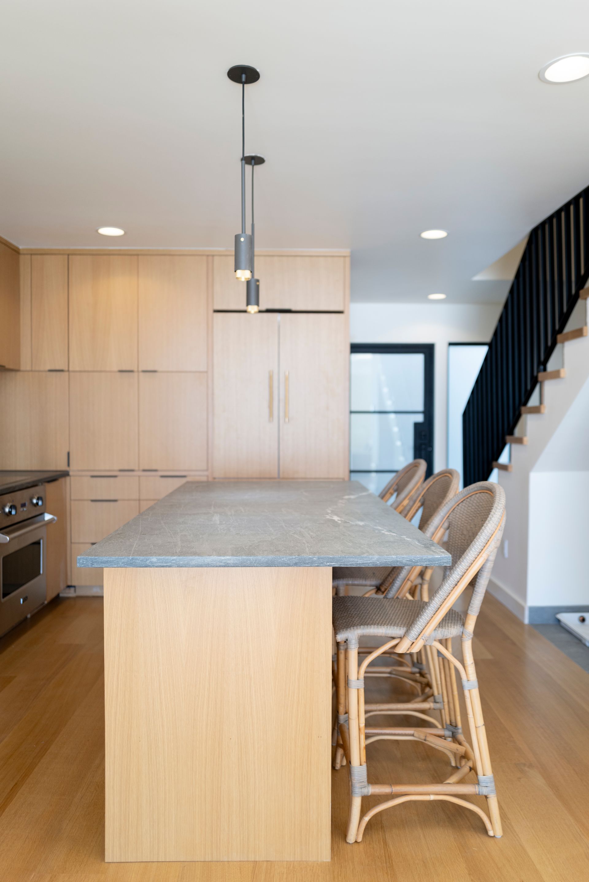 Modern kitchen with island, wood cabinets, pendant light, and staircase in the background