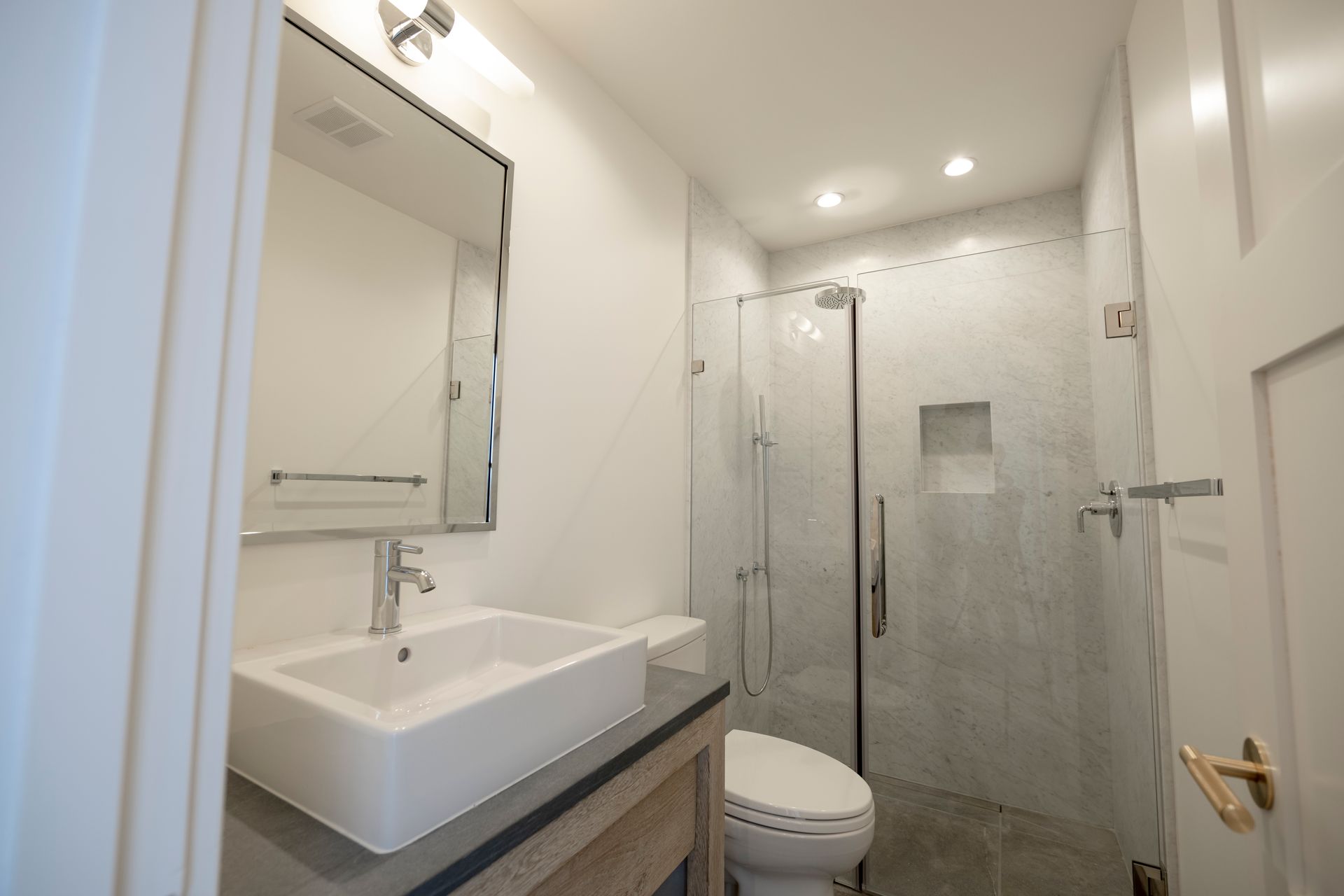 Small modern bathroom with white vanity, mirror, toilet, and glass shower enclosure