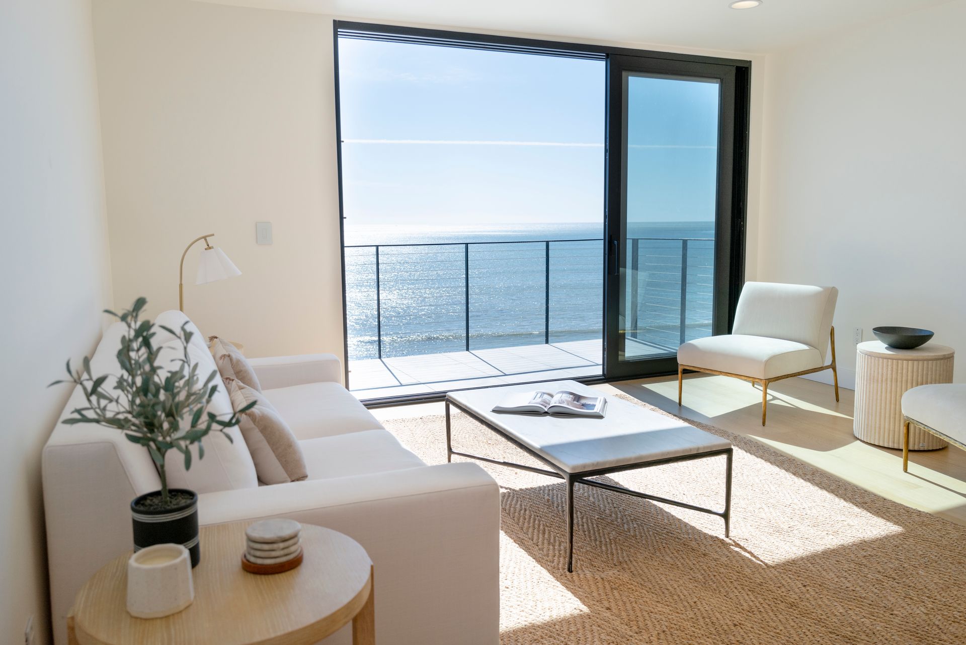 Bright living room with white furniture and a table overlooking the ocean through large sliding glass doors