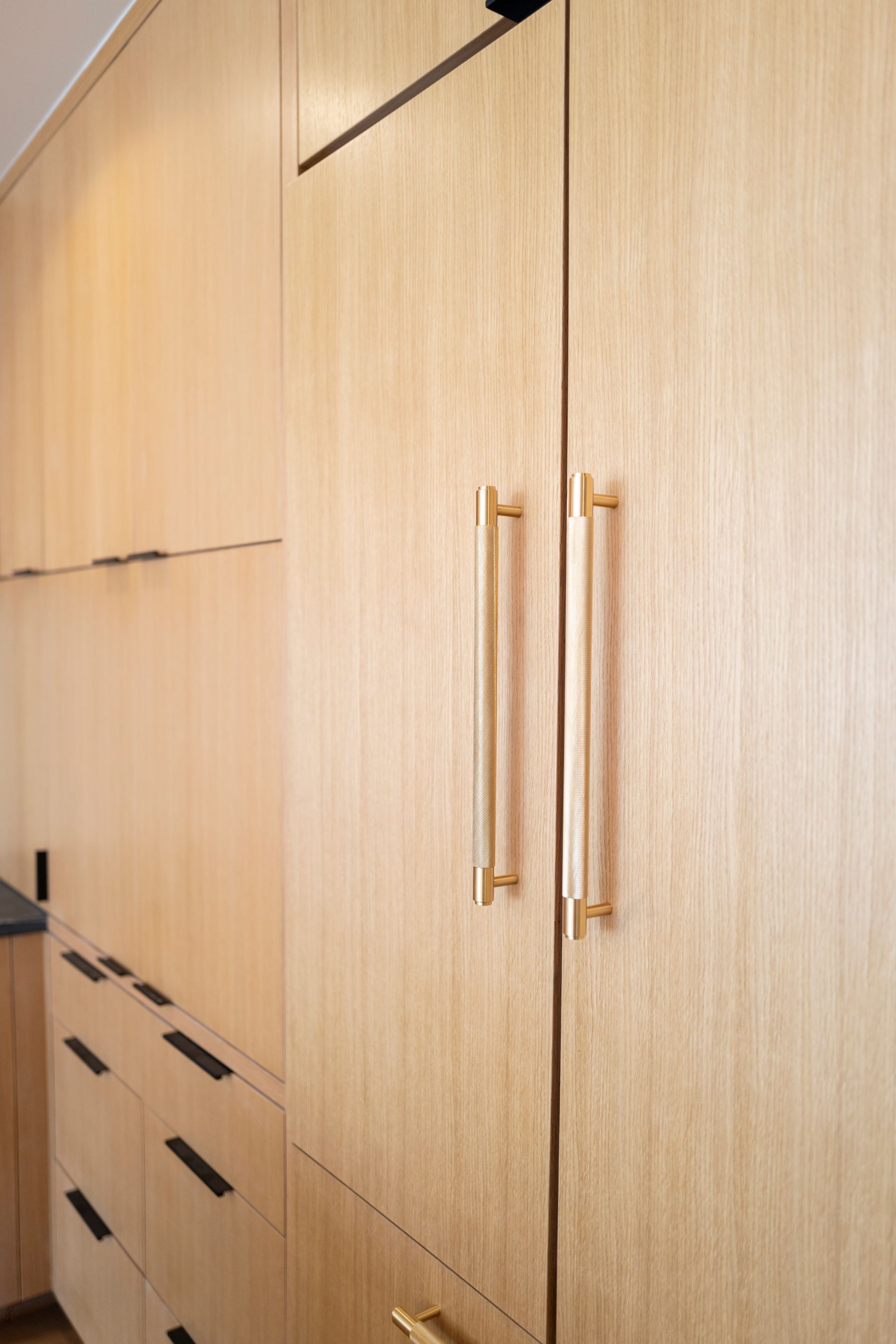 Wooden cabinet with long gold handles and drawers in a light wood room