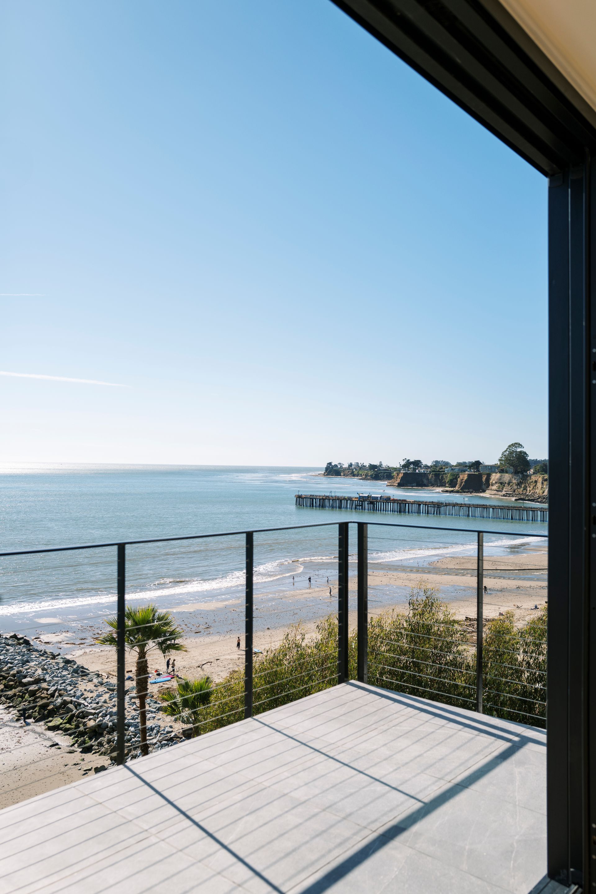 Balcony overlooking a sunny beach and ocean with a distant pier under a clear blue sky