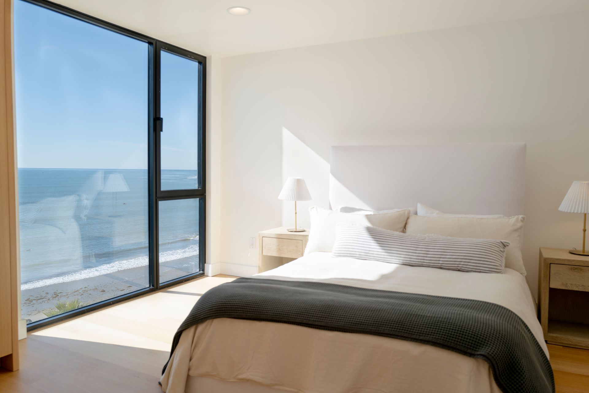 Bright bedroom with an ocean-view window, white bedding, and sunlight on the floor