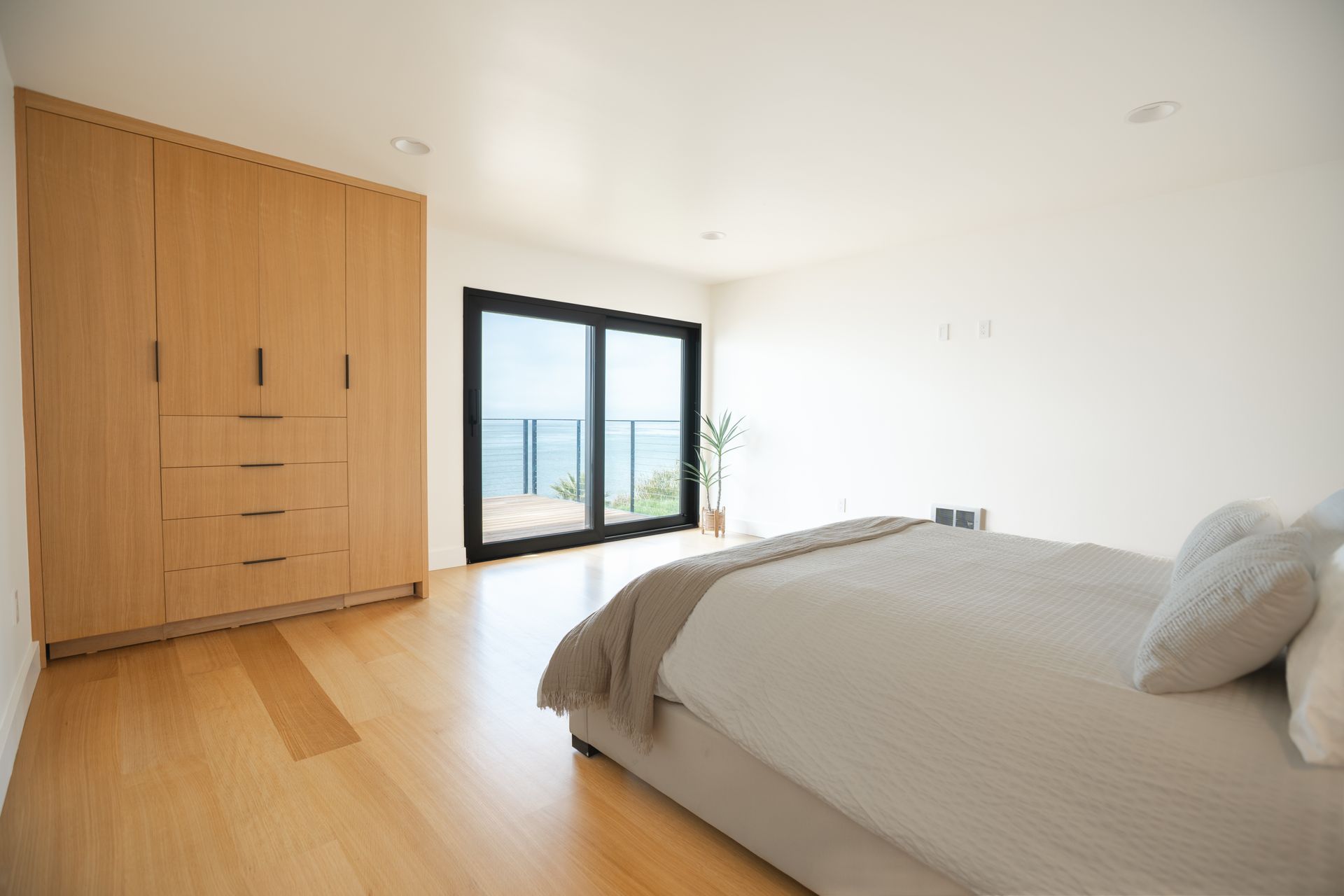 Bright minimalist bedroom with wooden wardrobe, bed, and large sliding glass doors overlooking a city view