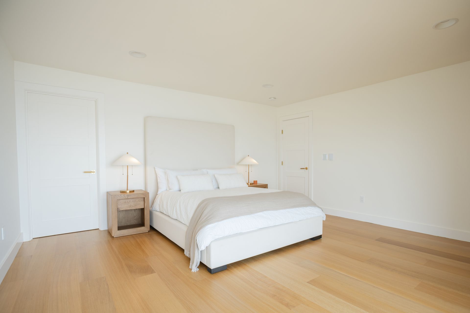 Minimal white bedroom with a bed, nightstands, and light wood floors