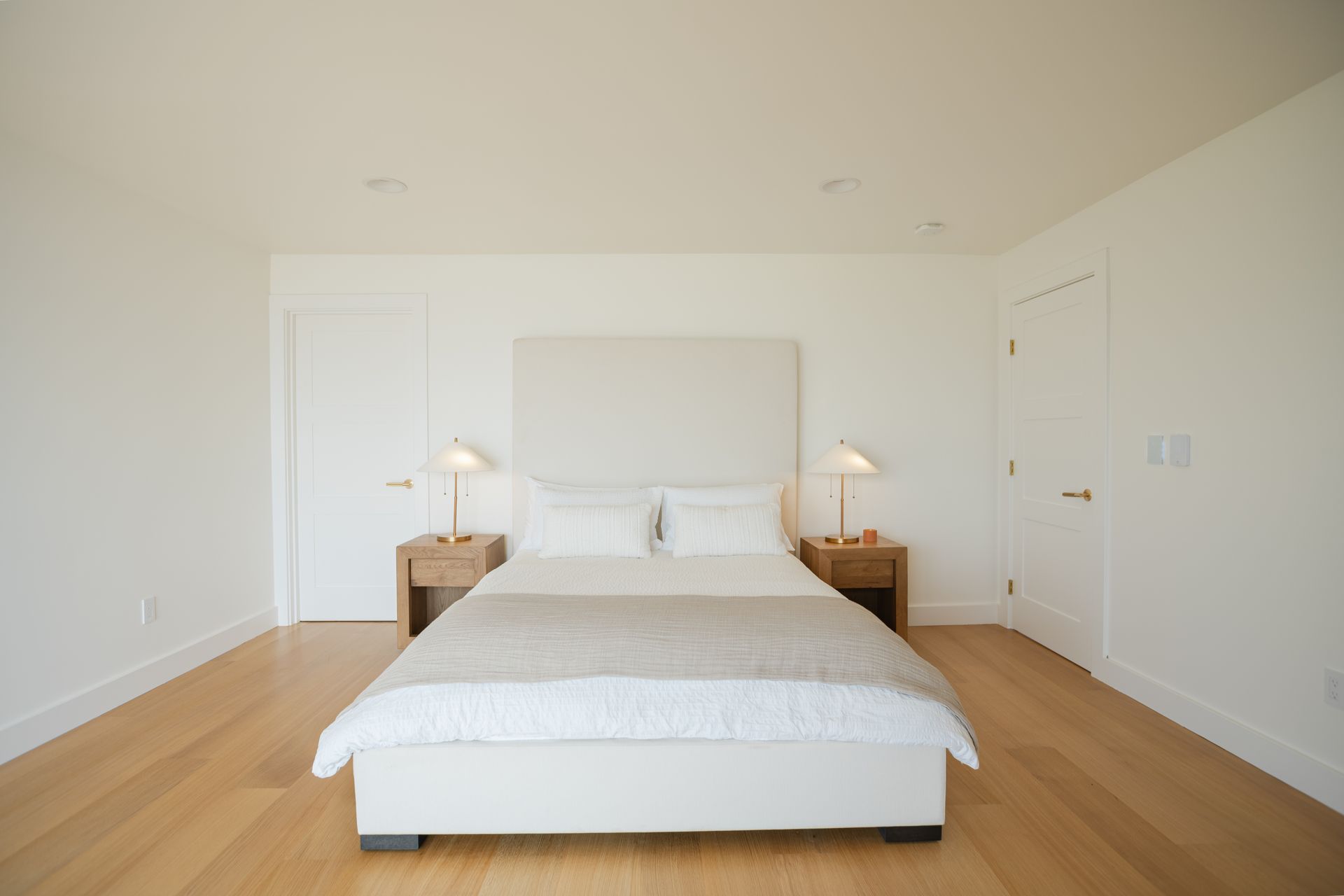 Bright minimalist bedroom with white bed, bedside lamps, and light wood floors