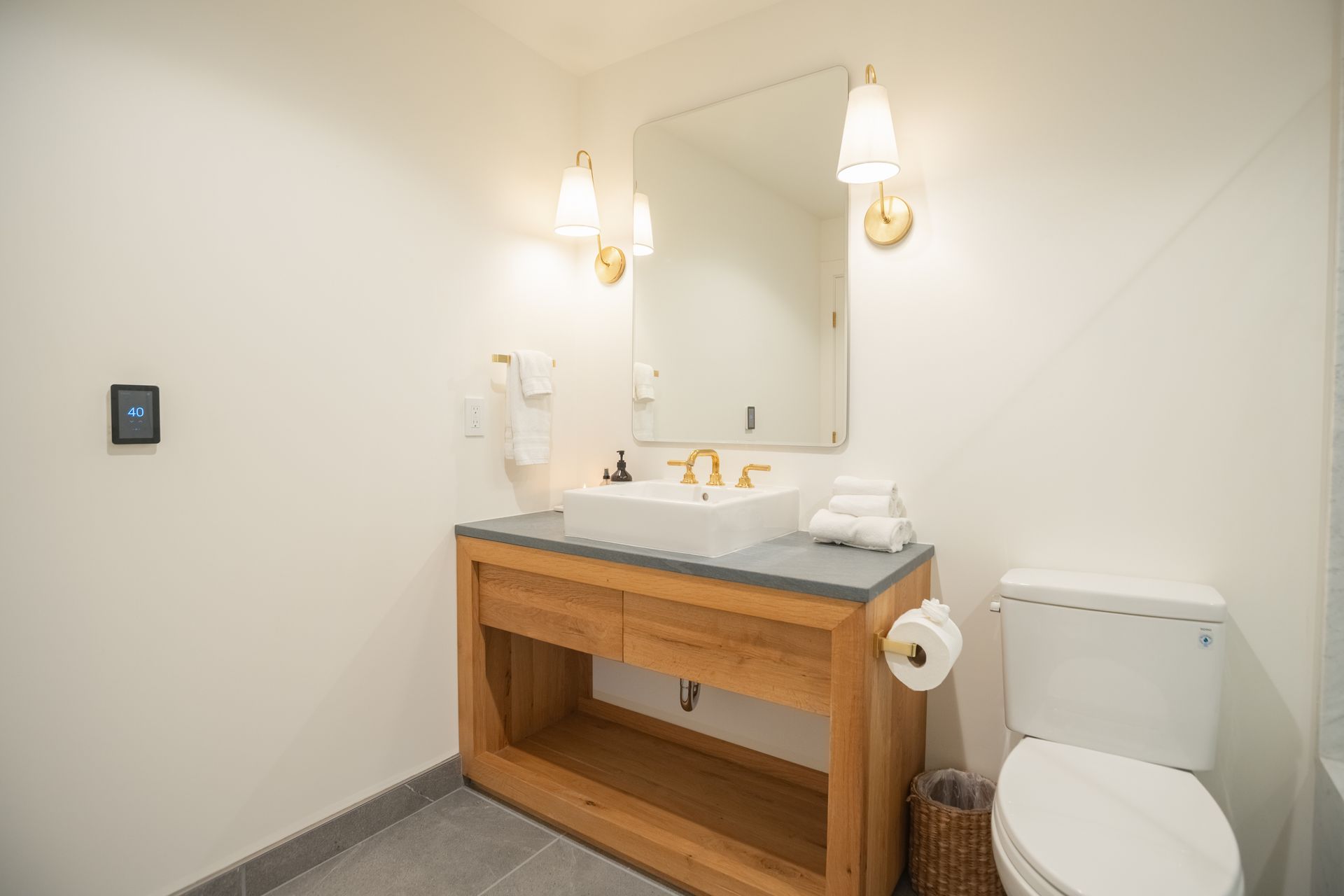 Modern bathroom vanity with mirror, sink, wall sconces, and toilet in a bright white room