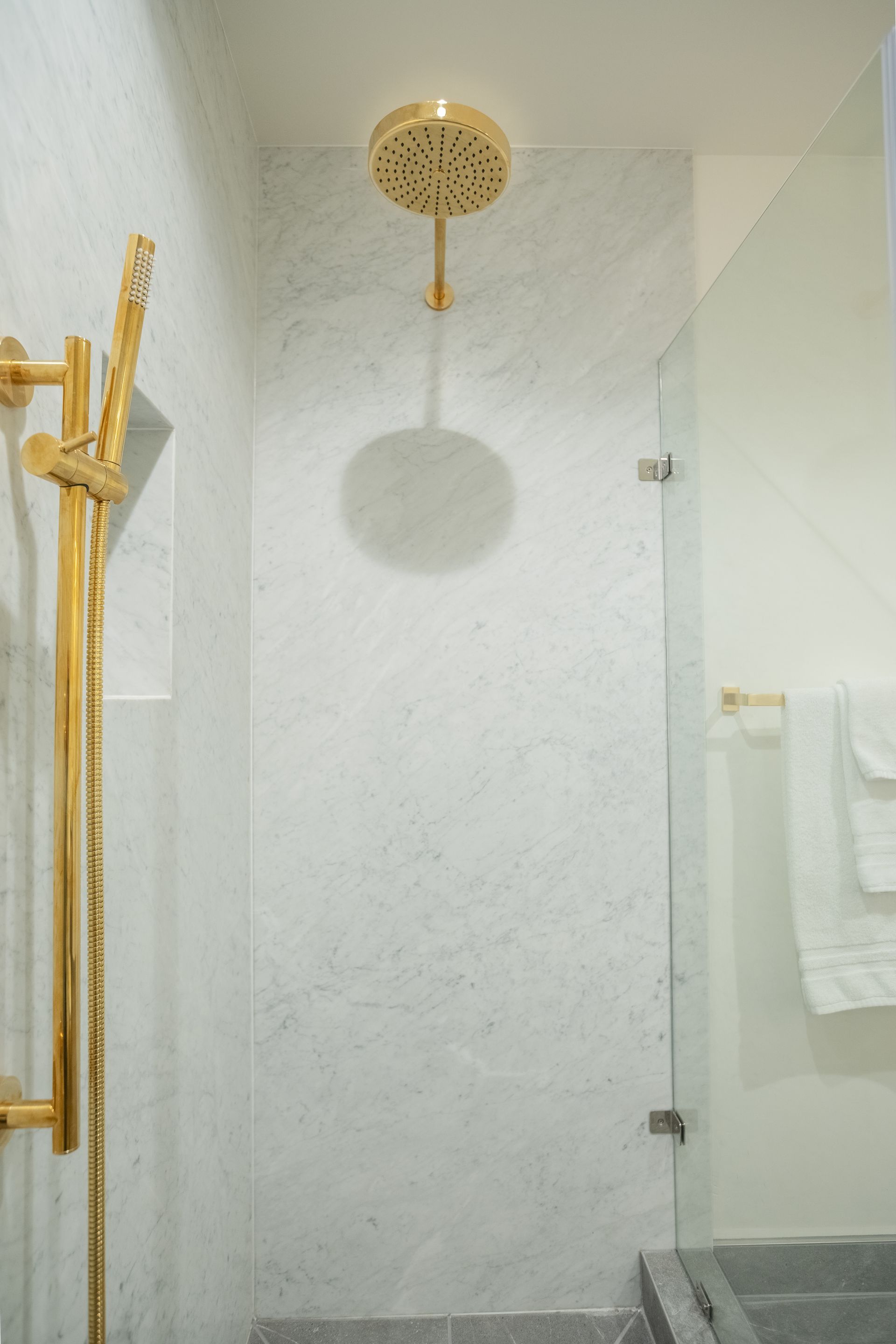 Modern bathroom shower with gold fixtures, white tiled walls, and a glass partition.