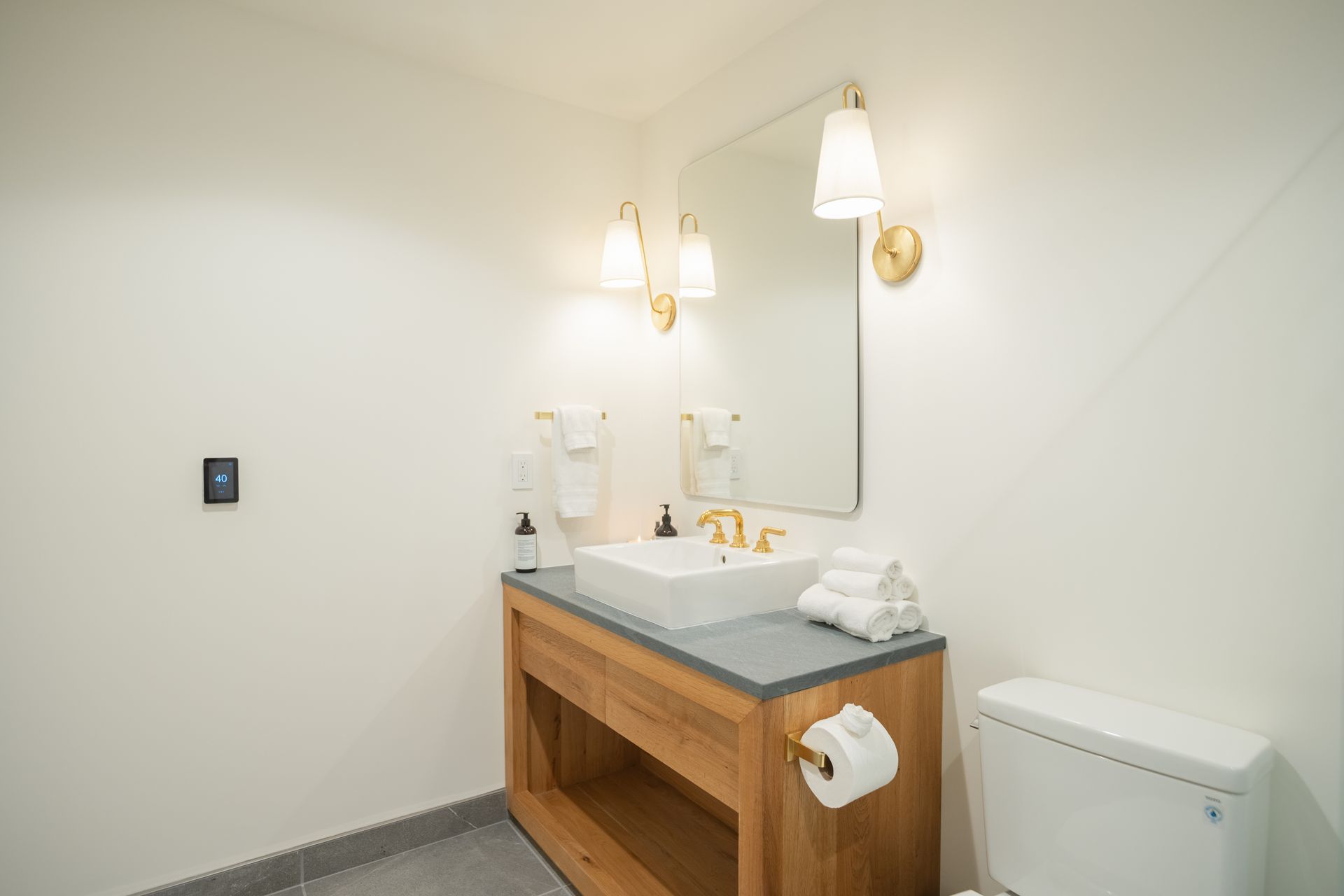 Modern bathroom vanity with sink, mirror, wall sconce, and towel holder against white walls