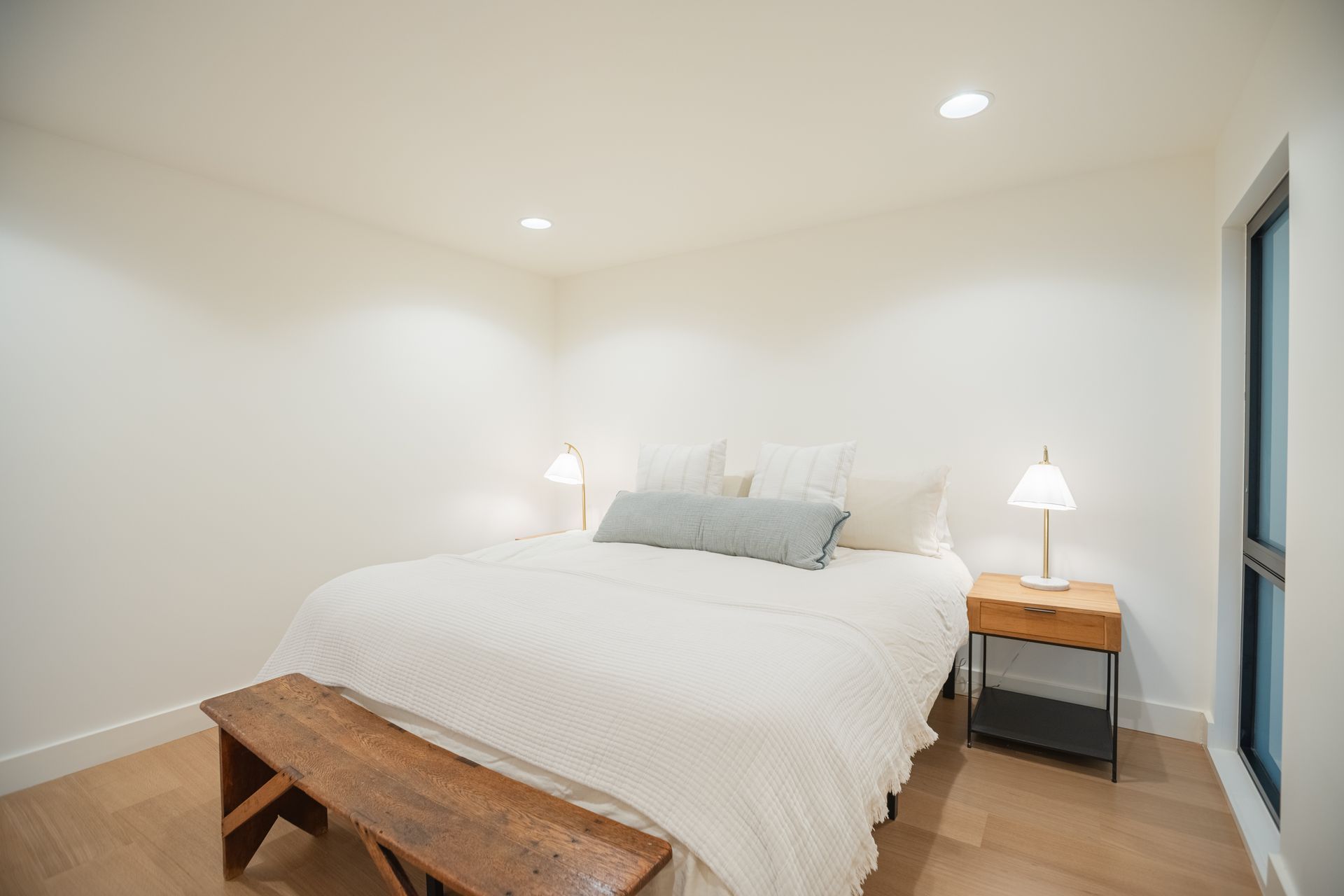 Bright bedroom with a large bed, bedside lamps, and a wooden bench at the foot of the bed.