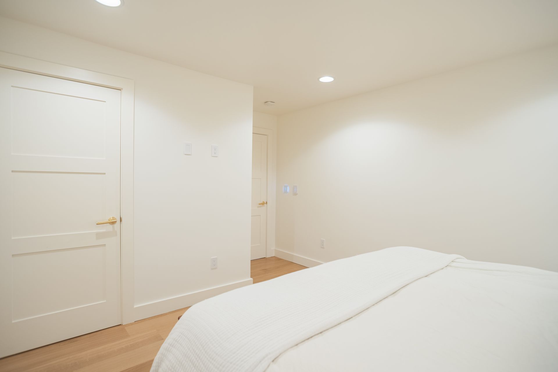 Bright, empty bedroom with white walls, a white door, and a bed with white bedding.
