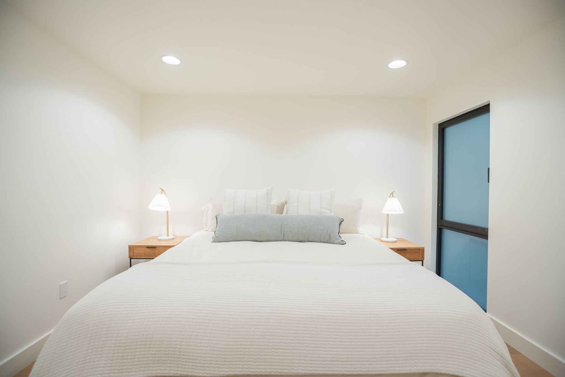 Minimal bedroom with a white bed, bedside lamps, and a blue door on the right