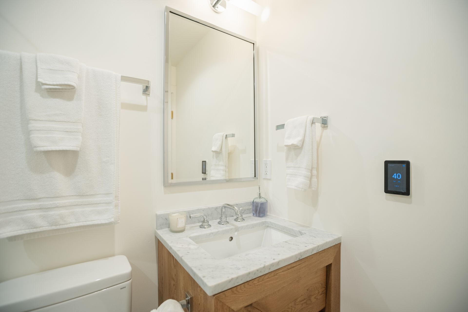 Bright bathroom vanity with mirror, white towels, and a wall-mounted touchscreen panel