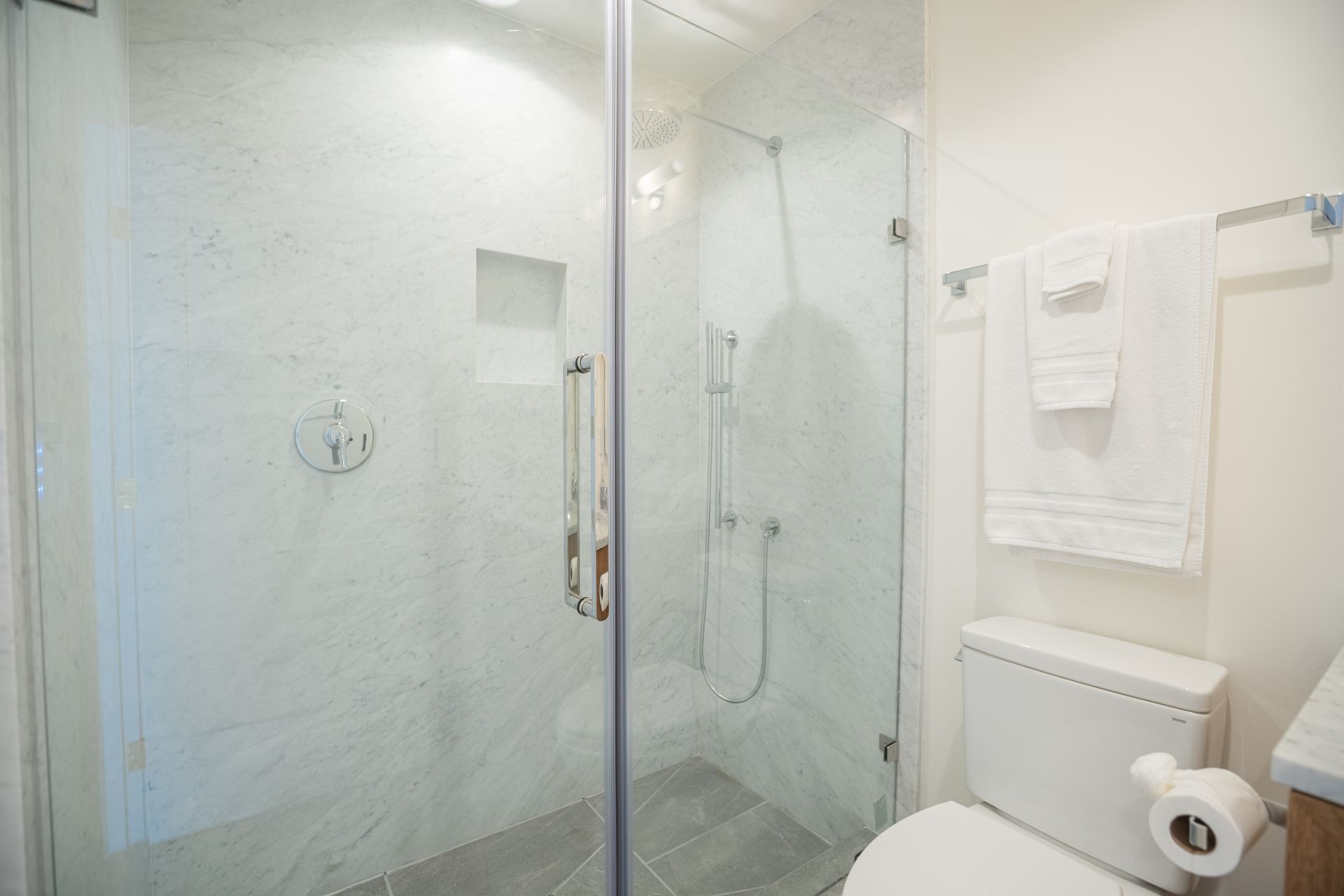 Modern bathroom with glass shower enclosure, white towels, and toilet paper holder