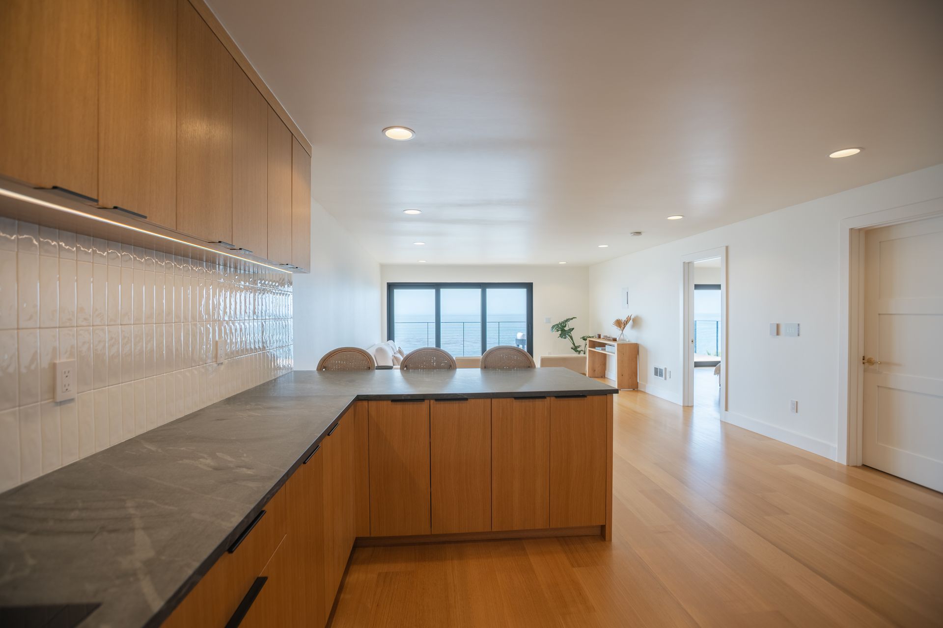 Modern kitchen with wood island, gray countertops, white tile backsplash, and bright open dining area.