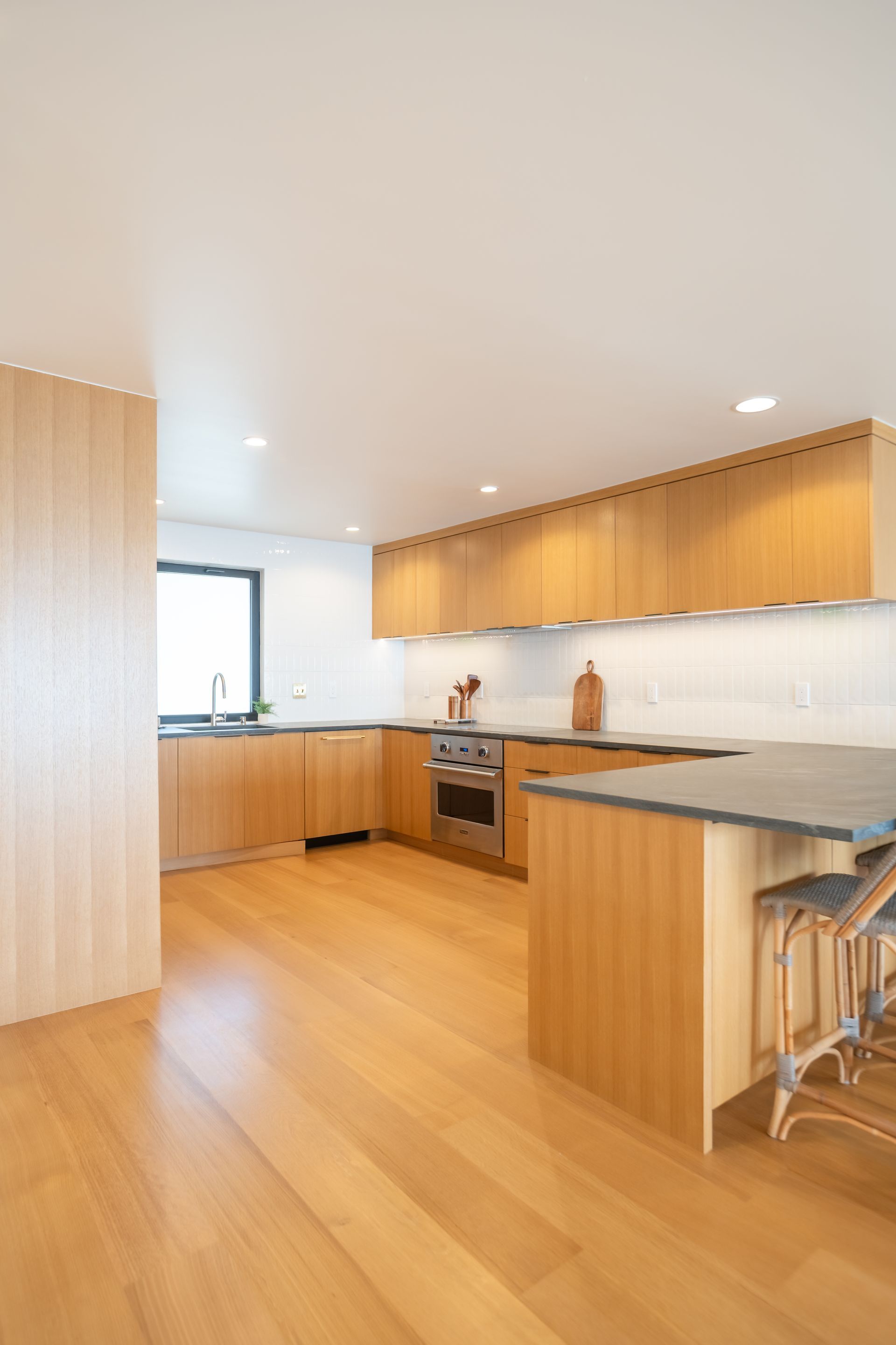 Bright modern kitchen with wood cabinets, light wood floors, white tile, and a central island with bar stools