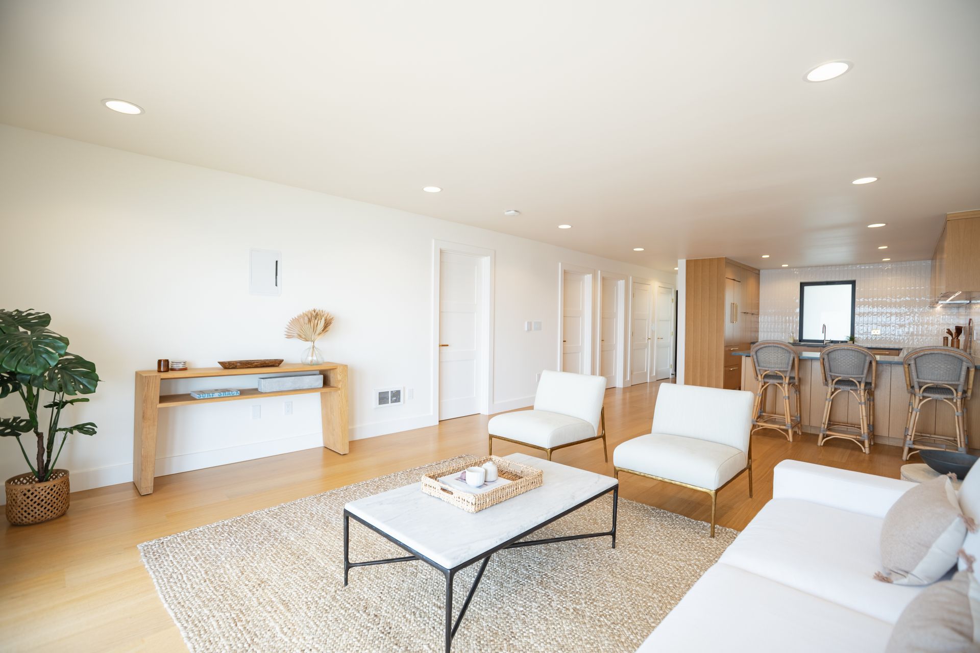 Bright modern living room with white chairs, coffee table, console, and open kitchen/dining area