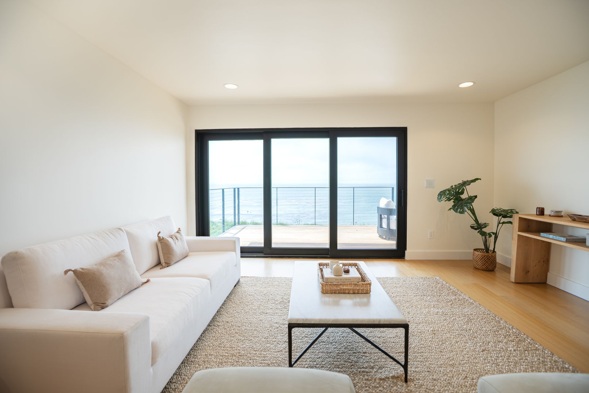 Bright modern living room with white sofa, coffee table, wood floor, and ocean-view balcony windows