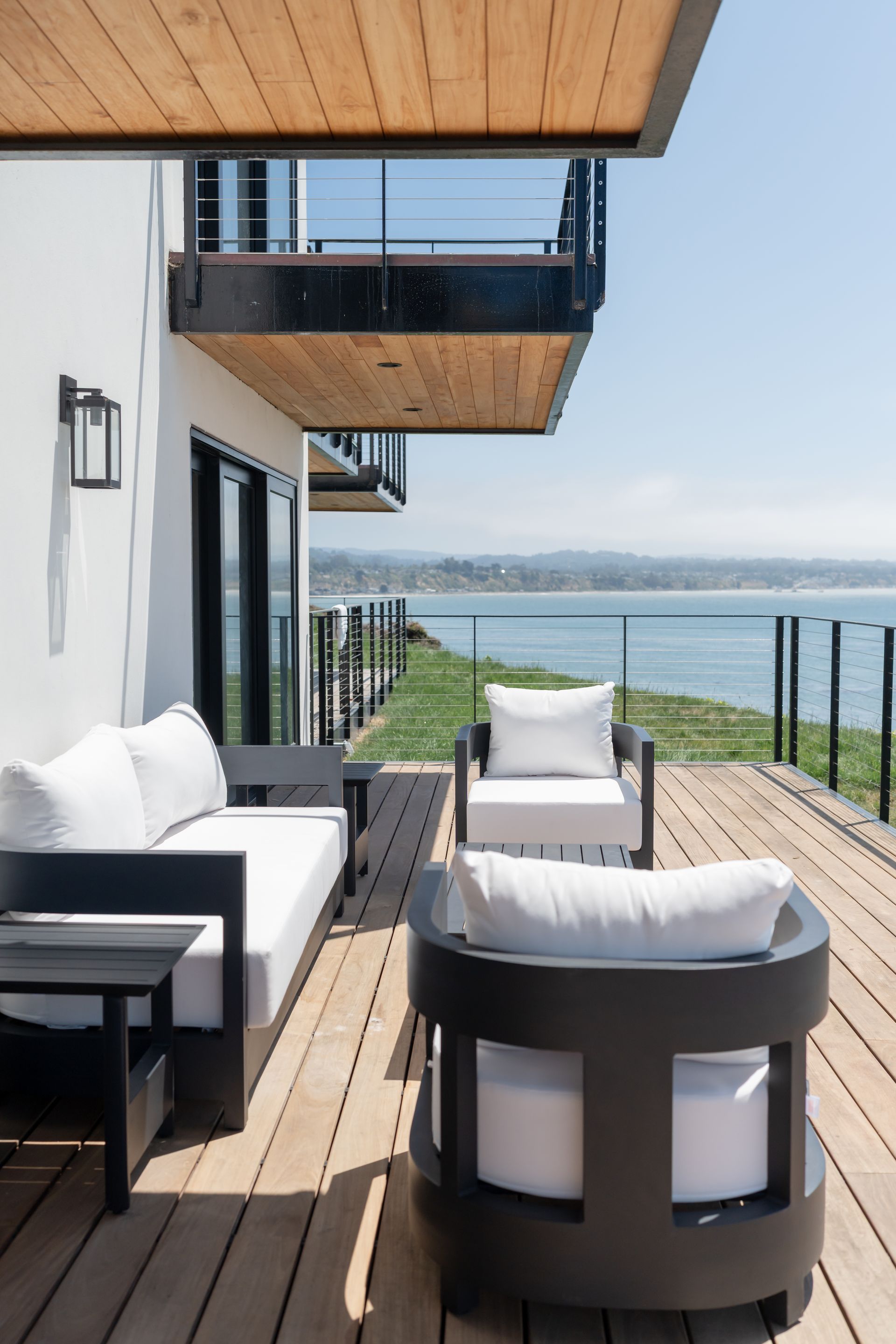 Modern waterfront deck with white lounge chairs and black railings overlooking the water