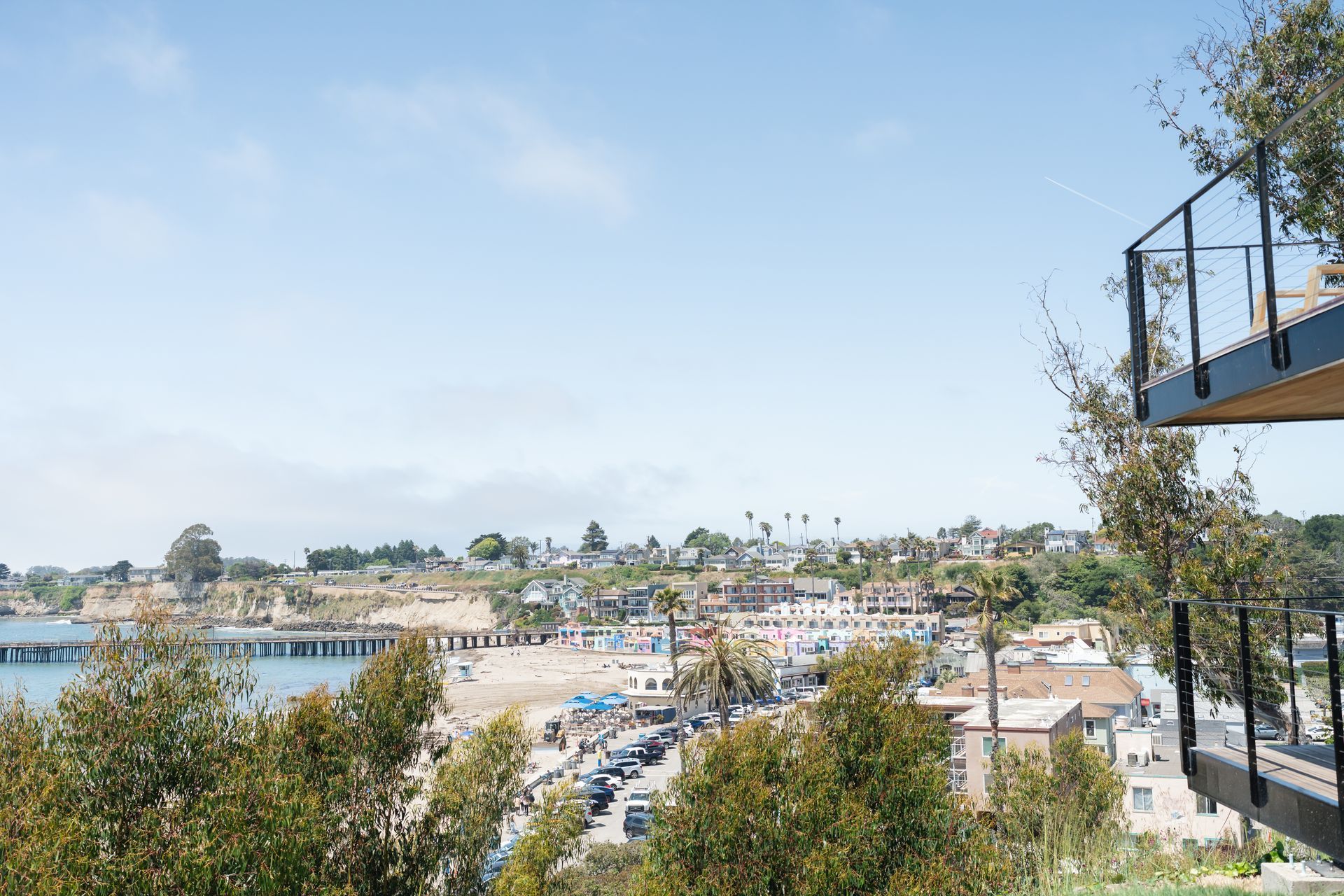 Sunny coastal town view with beach, buildings, and trees under a clear blue sky