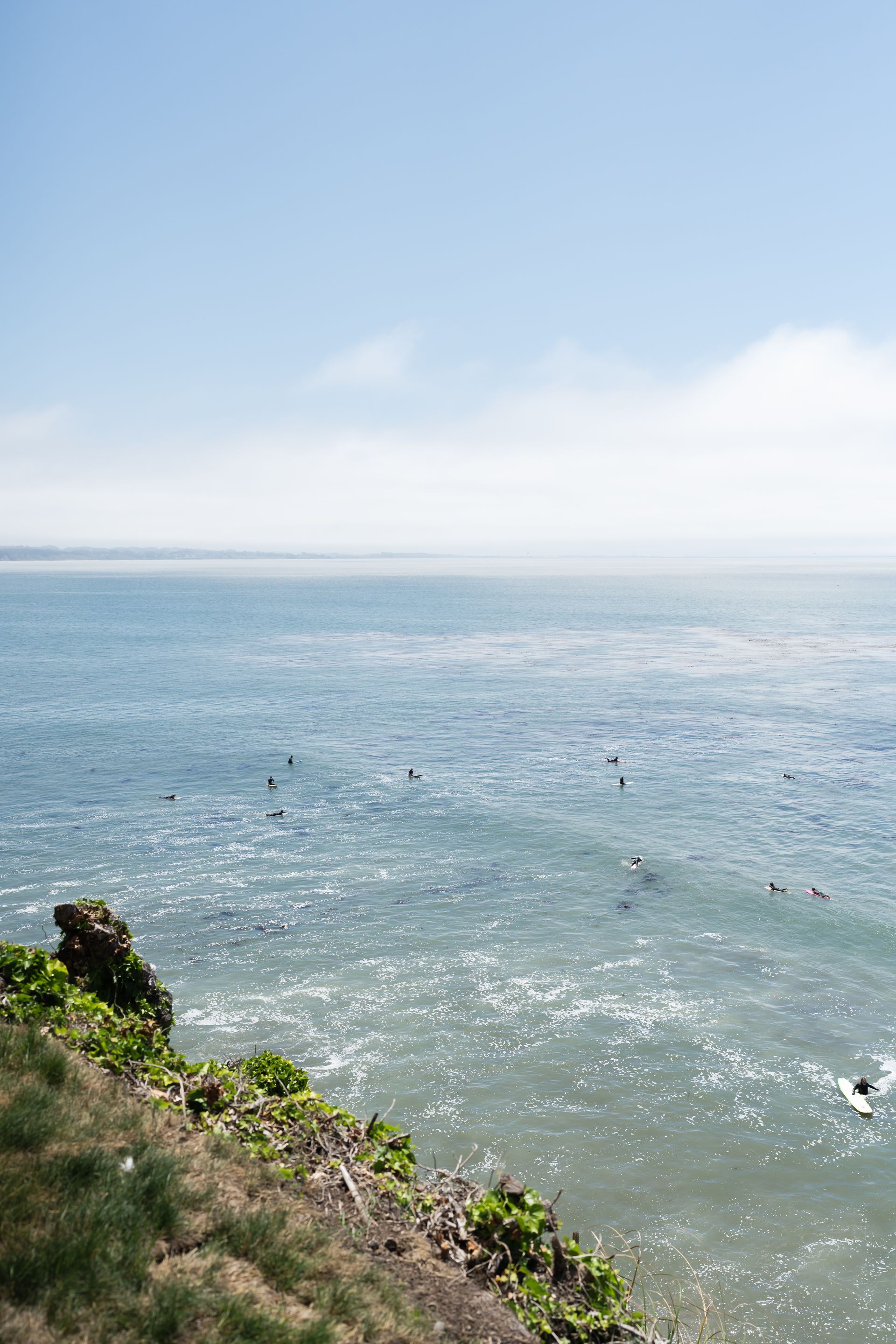 Coastal view of sparkling blue ocean under a pale sky, with grassy shoreline in the foreground