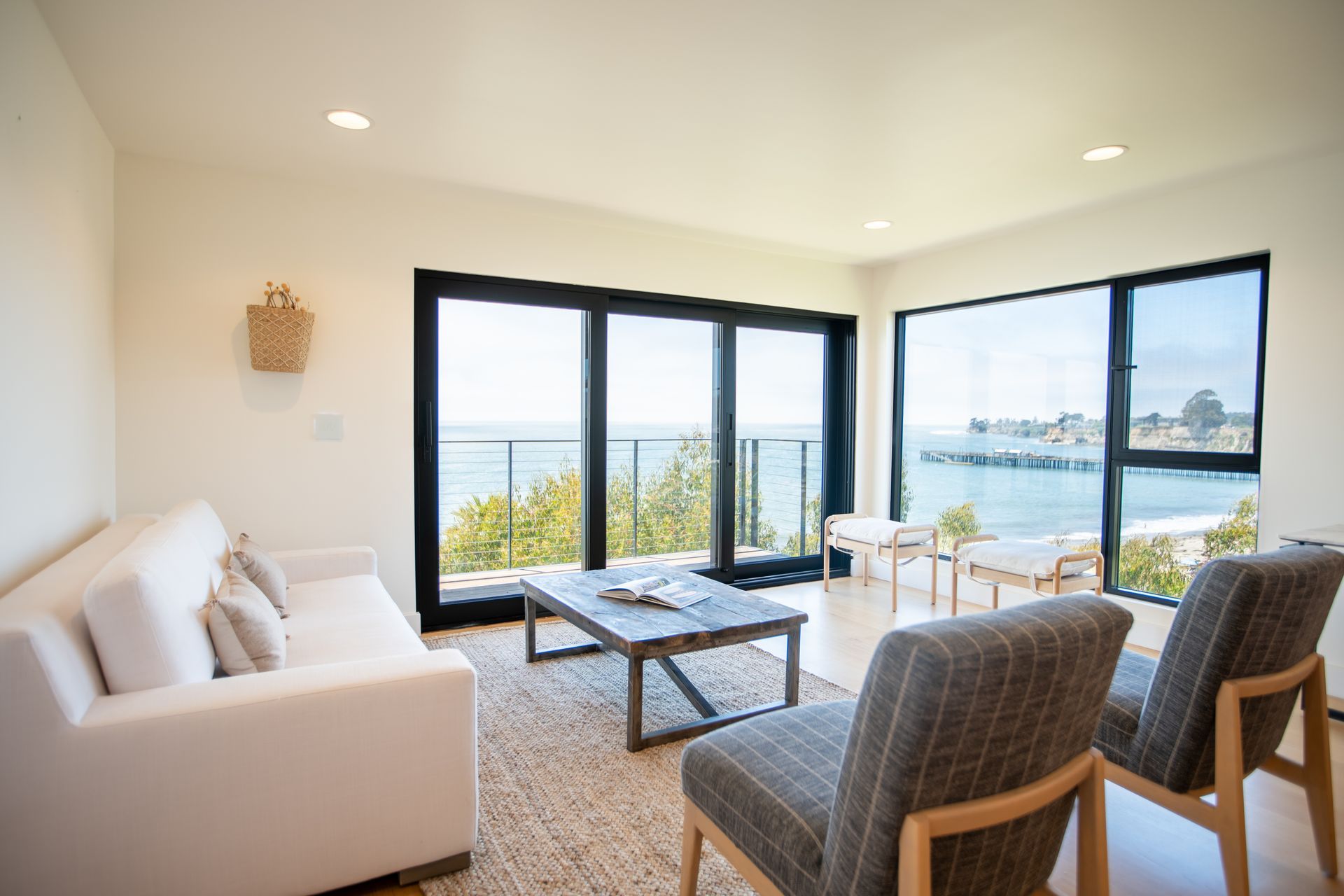 Bright modern living room with ocean view, white sofa, woven chairs, and large windows